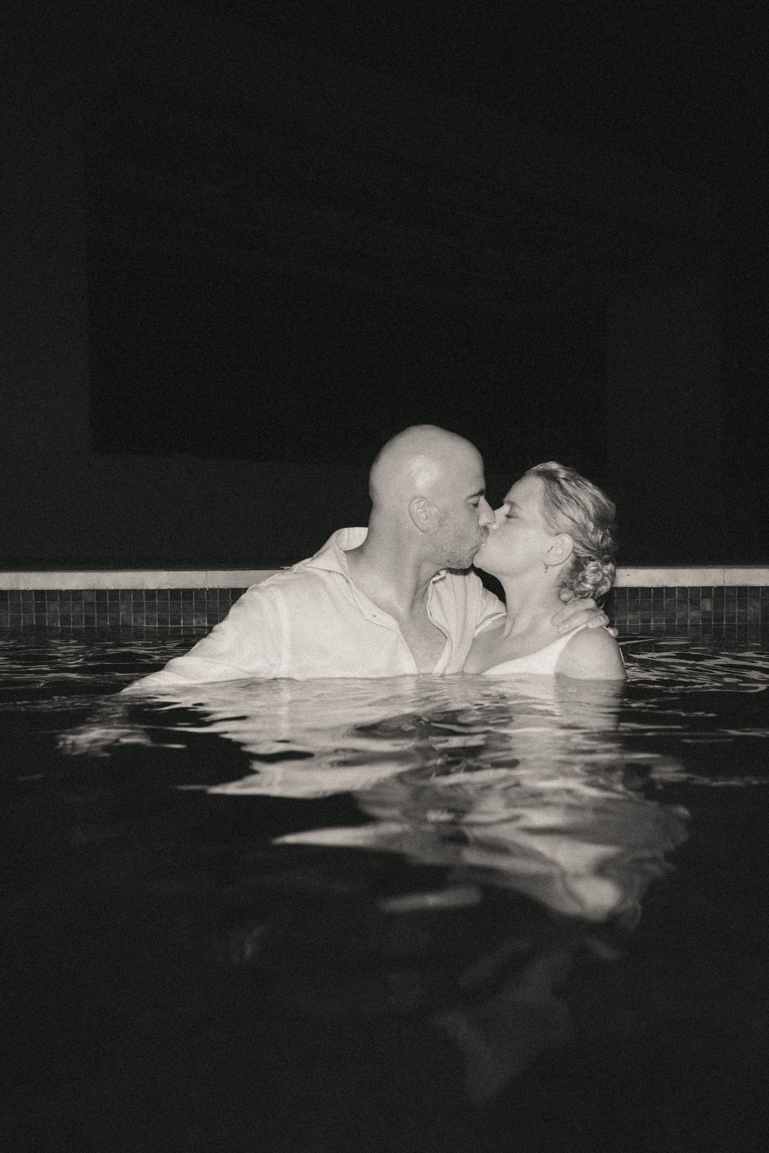 Artistic black and white photo of a couple floating in water wearing wedding attire.
