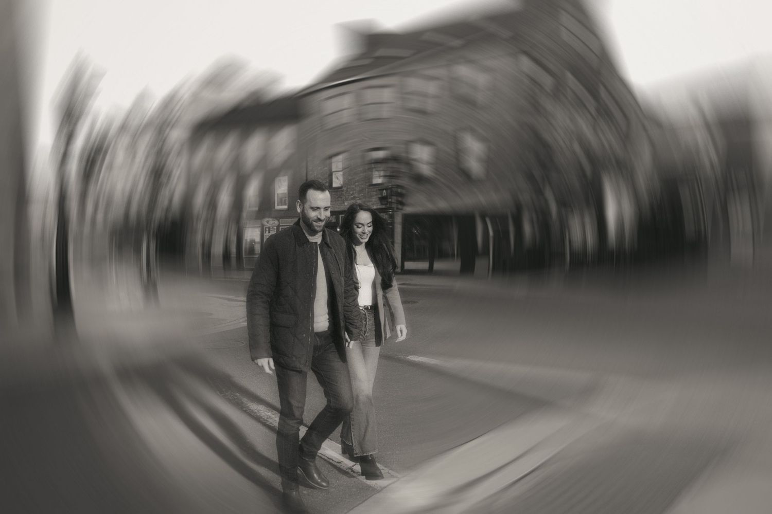 Black and white photo of a couple walking together on a city street with a dreamy radial blur effect.
