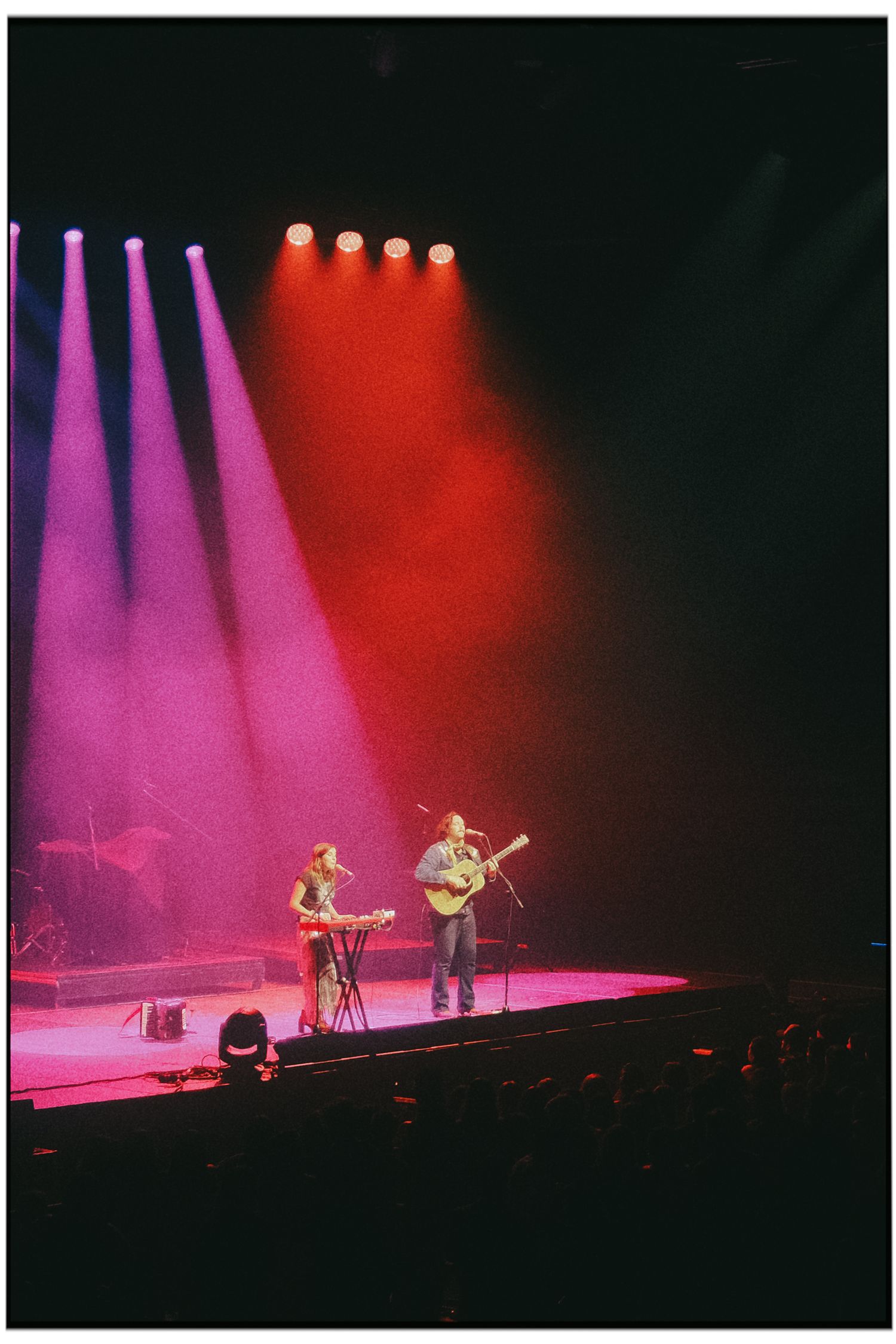 Concert performers on stage with dramatic pink and red lighting effects creating a moody atmosphere during live performance.