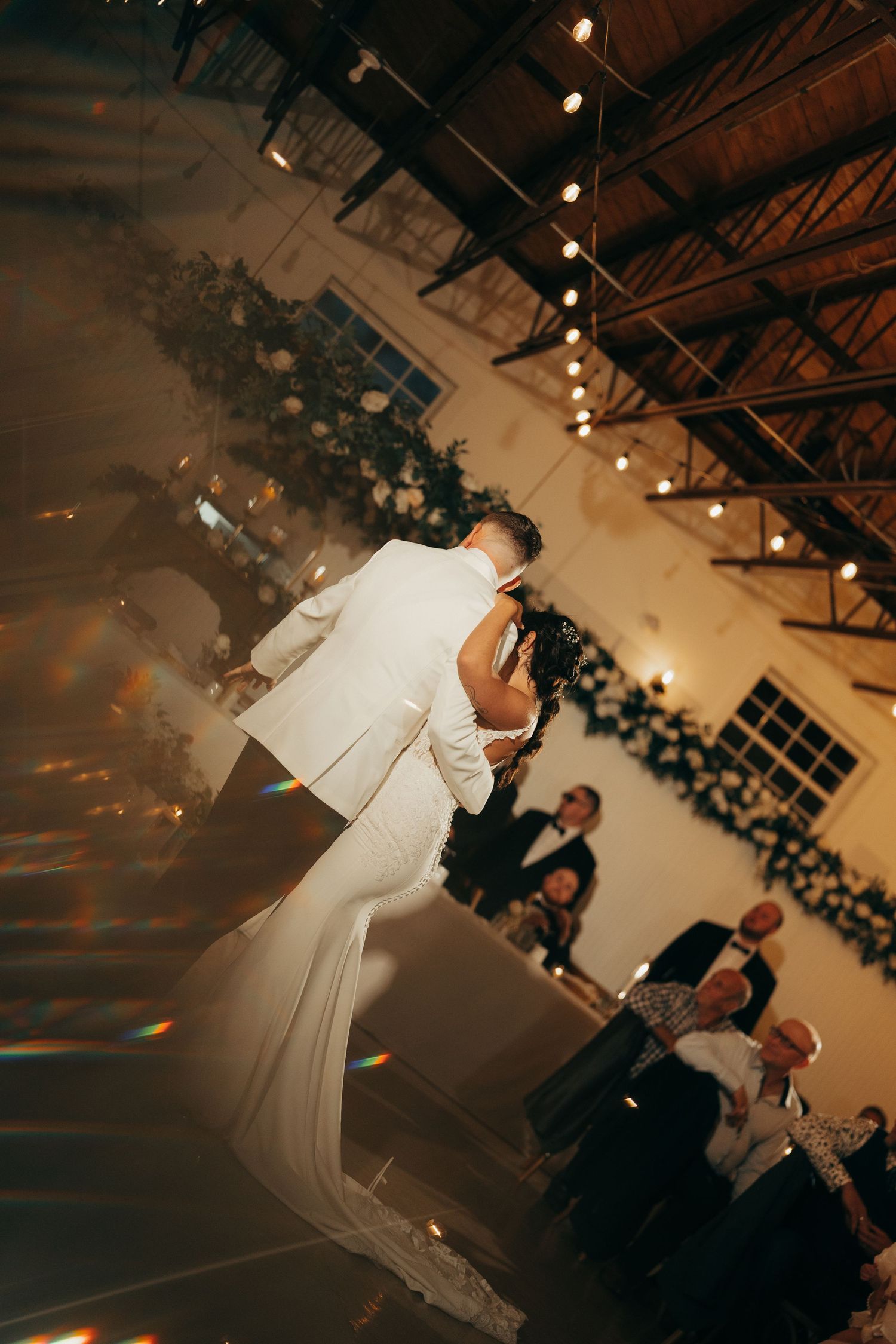 A couple shares their first dance at a wedding reception under warm lighting in an industrial-style venue.
