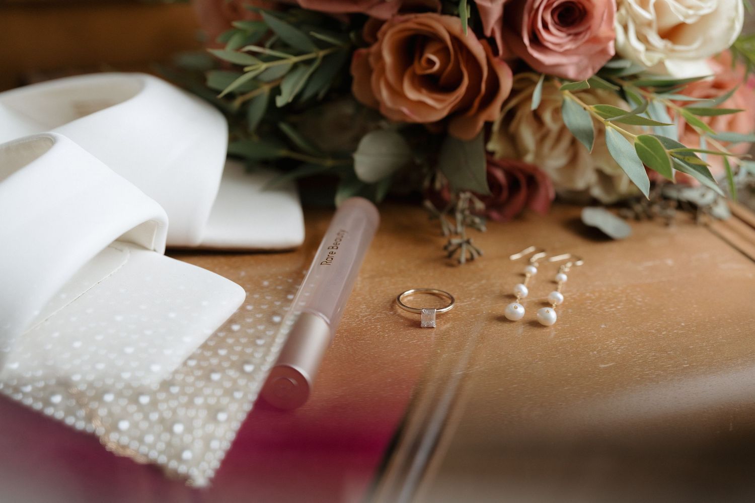 Wedding rings and floral arrangements displayed on a rustic wooden surface with delicate pink roses and greenery.