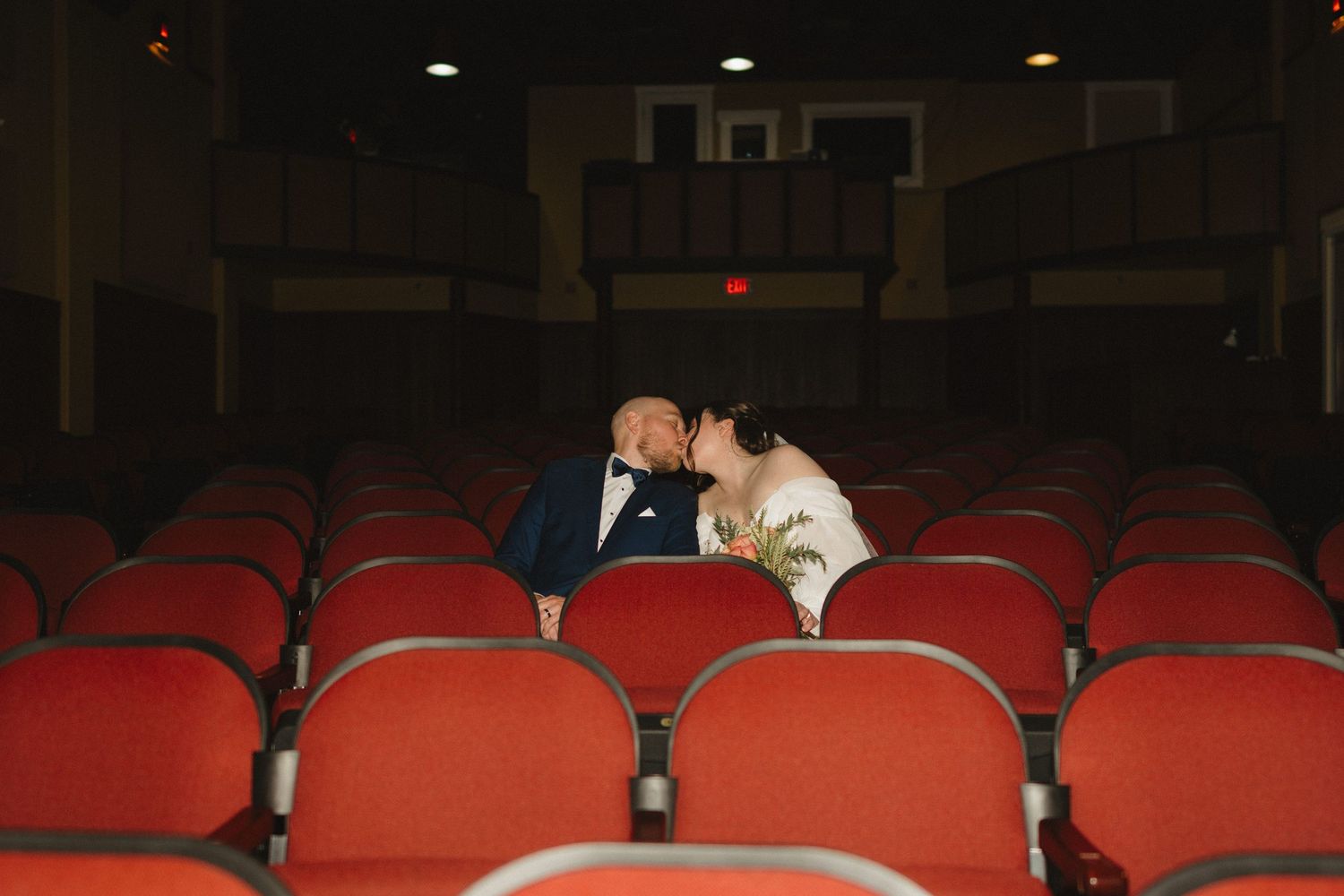 Empty red theater seats arranged in rows inside a dimly lit auditorium.