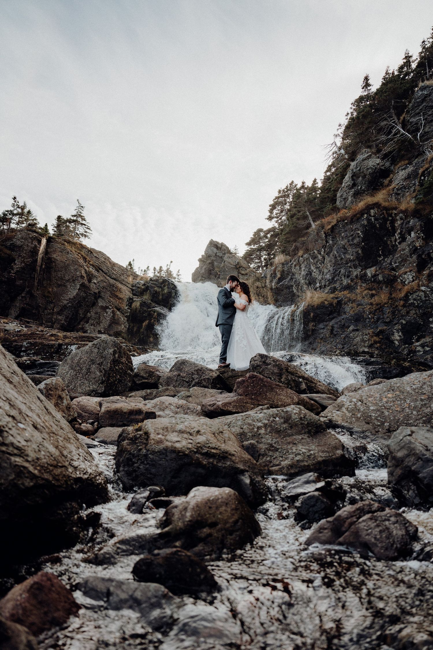 A dramatic series of cascading waterfalls flowing over dark rocky cliffs surrounded by evergreen trees in winter.