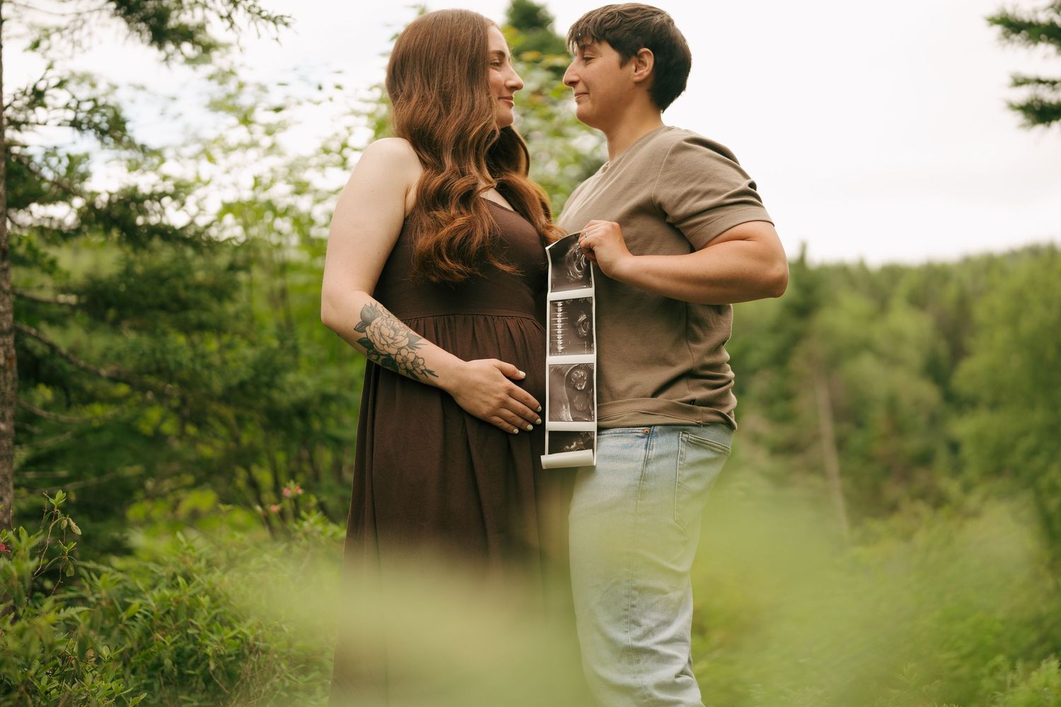 Couple holding ultrasound photo outdoors in lush green forest during maternity announcement photography session.