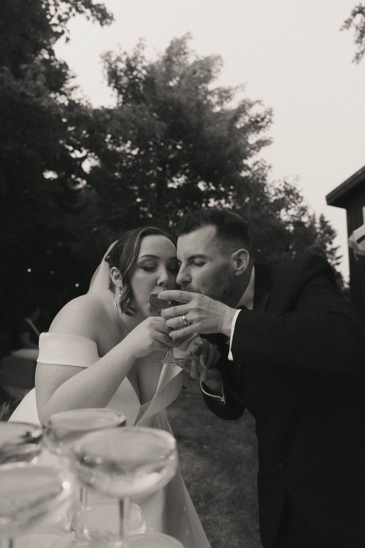 Newlyweds share an intimate moment while sipping champagne at an outdoor wedding reception.