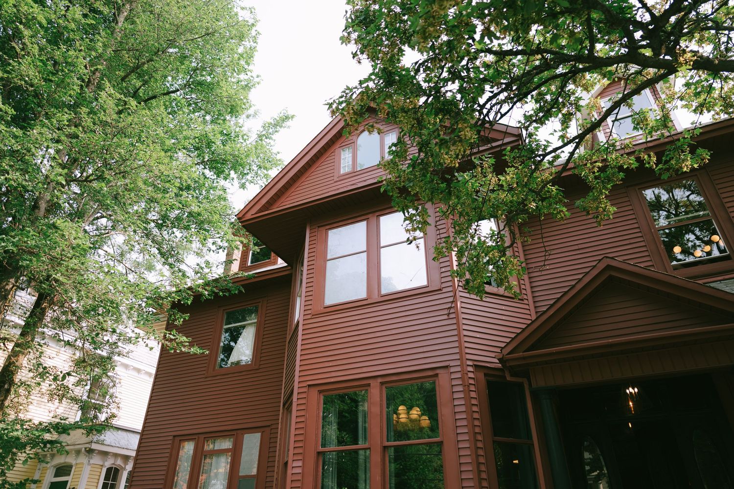 Exterior view of traditional red wooden house surrounded by trees.