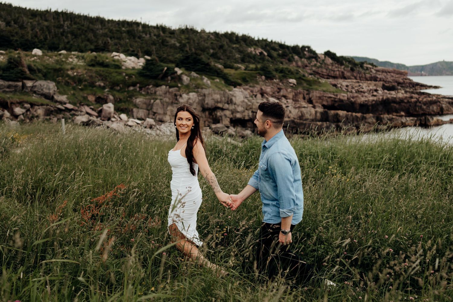 A couple shares a romantic moment on a rocky coastal cliff with ocean views in the background.