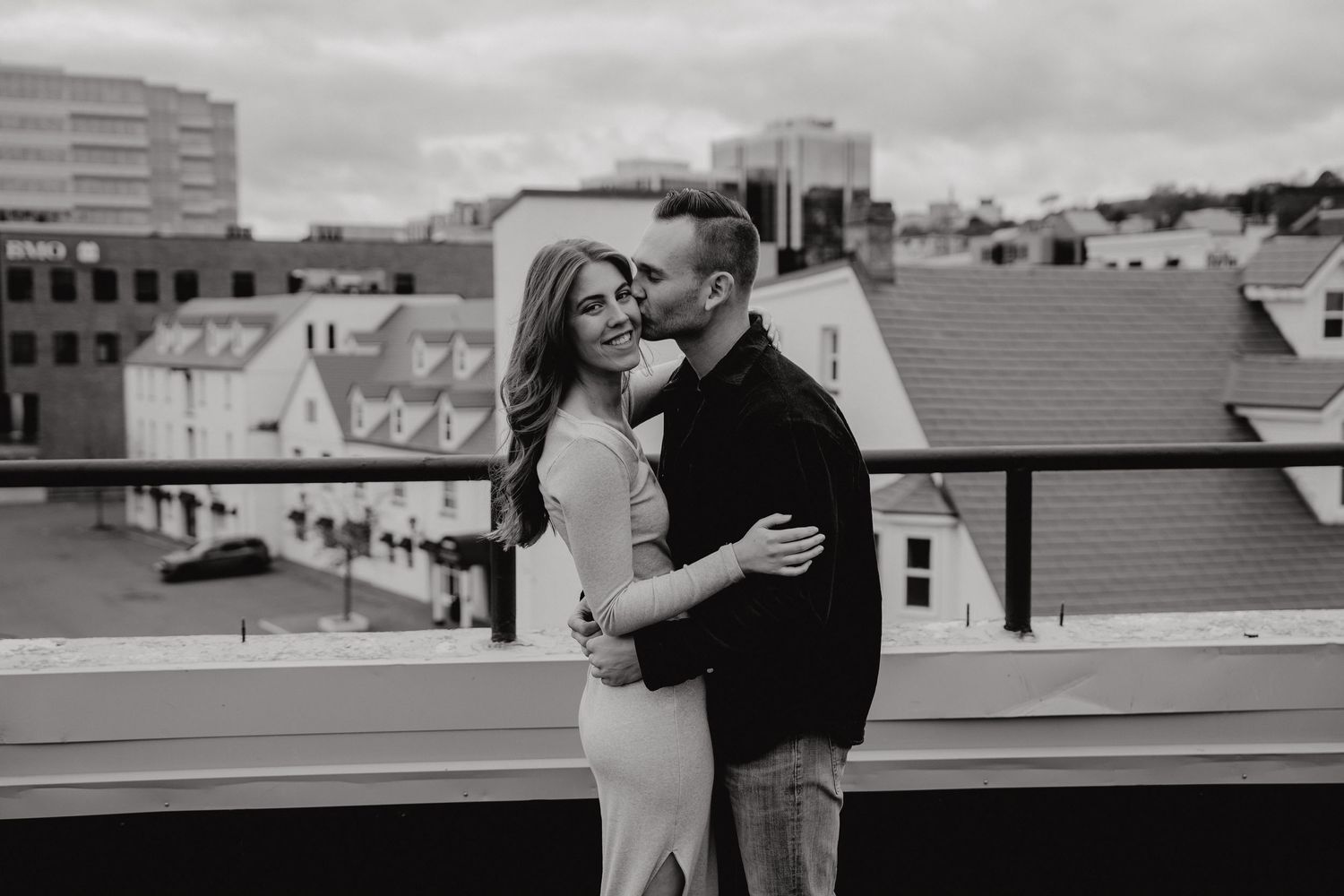 A black and white photo of two people in a loving embrace on a city rooftop.