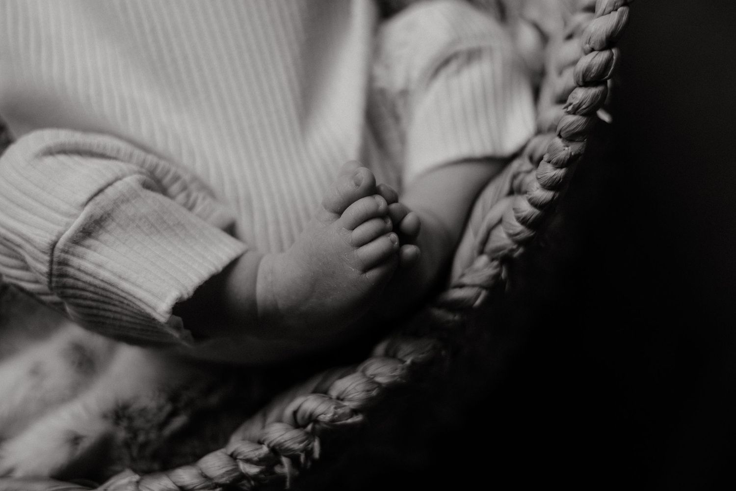 Artistic monochrome shot of an infant resting in a textured bassinet.