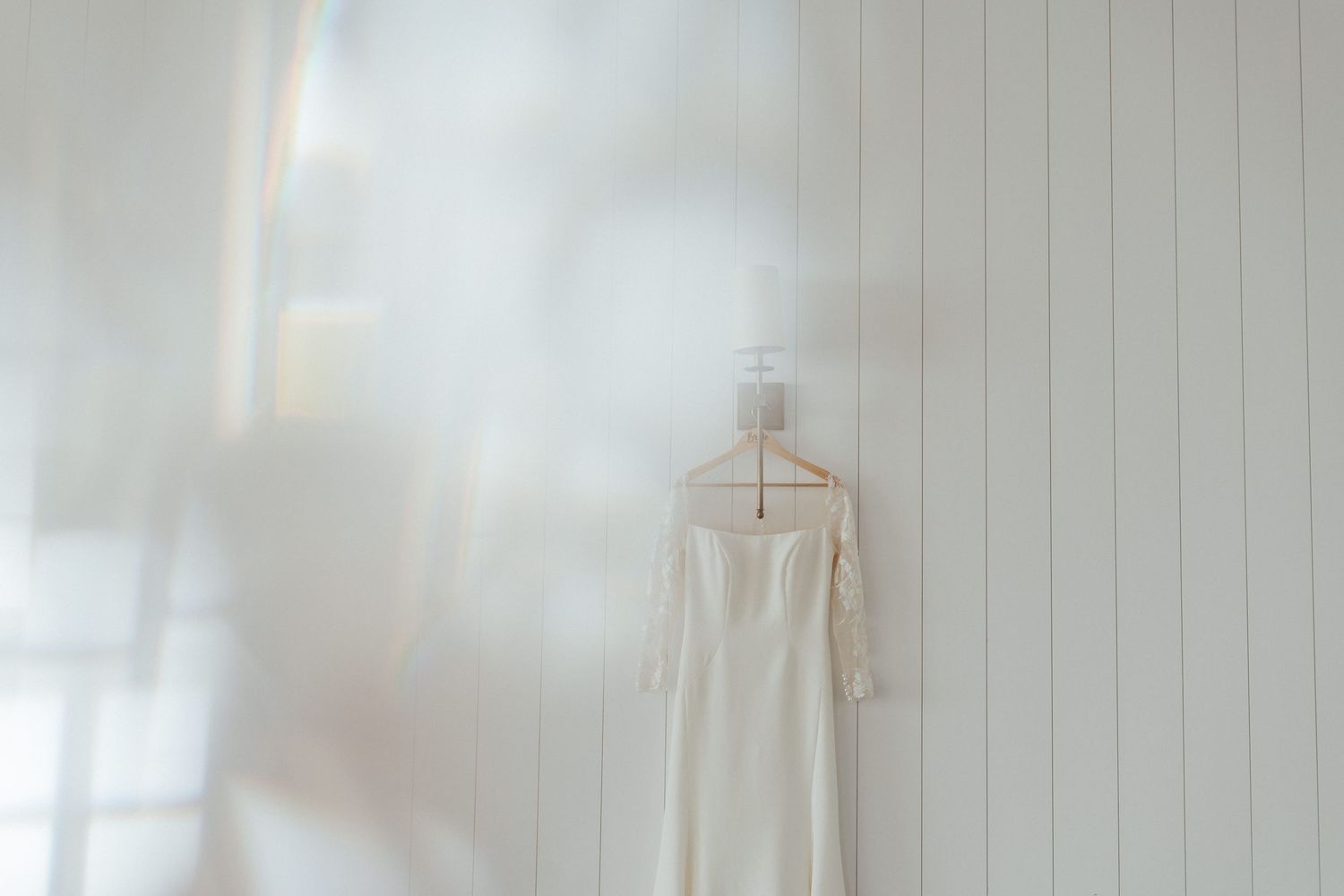 White wedding dress hanging against a light colored wall.