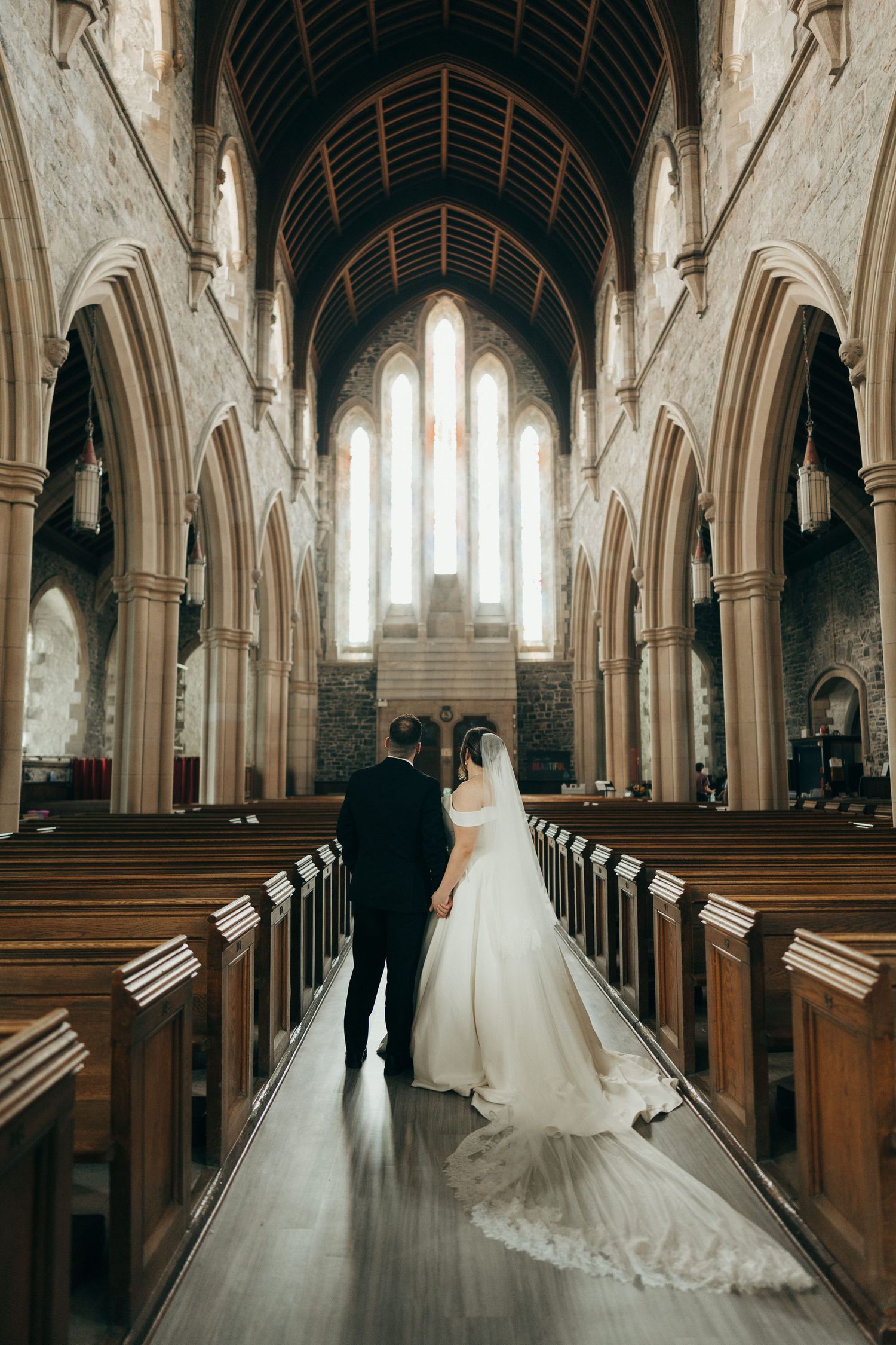 Wedding couple silhouetted in a majestic cathedral aisle with soaring stone columns.