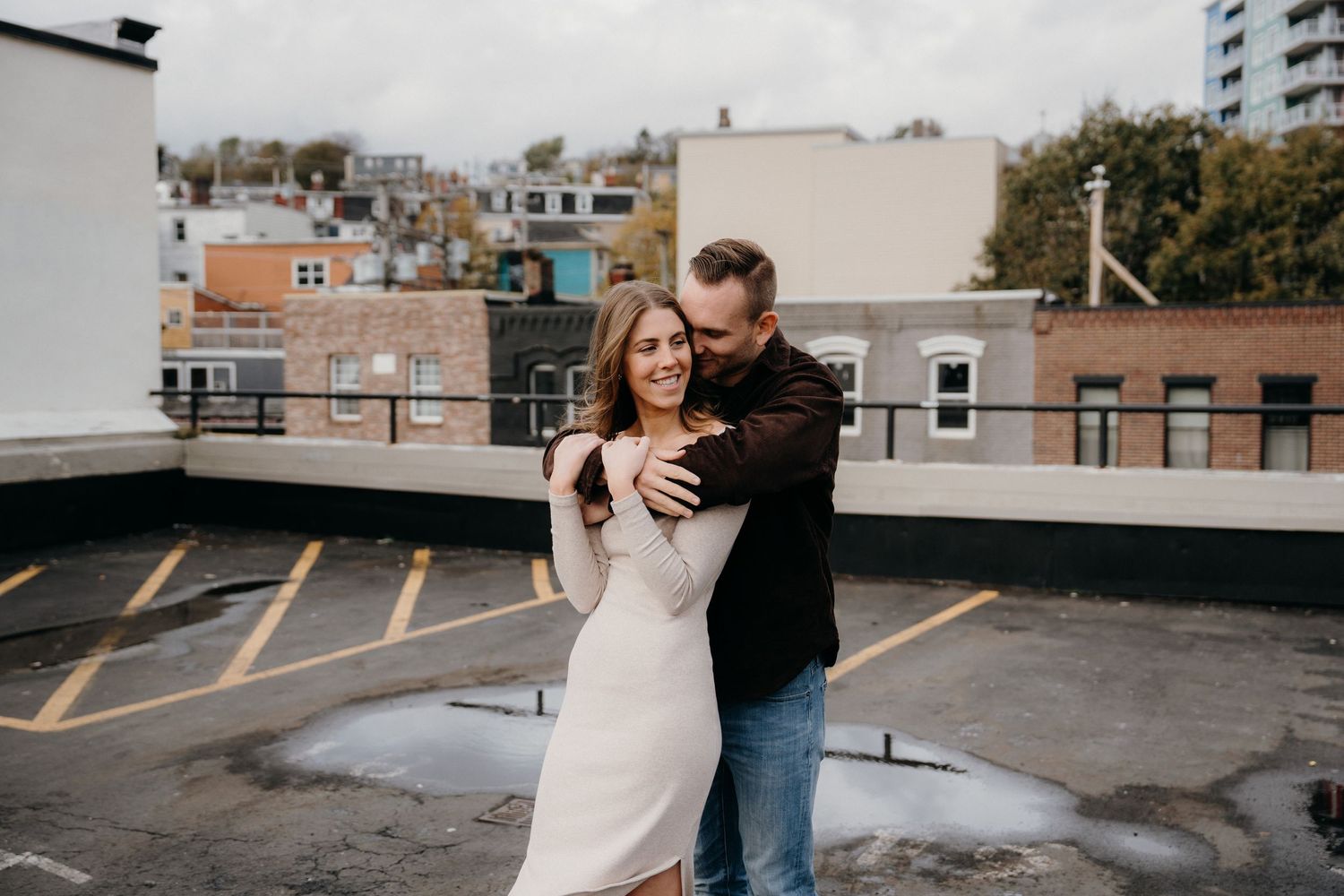 Sweet candid moment captured between couple on rooftop with cityscape backdrop.