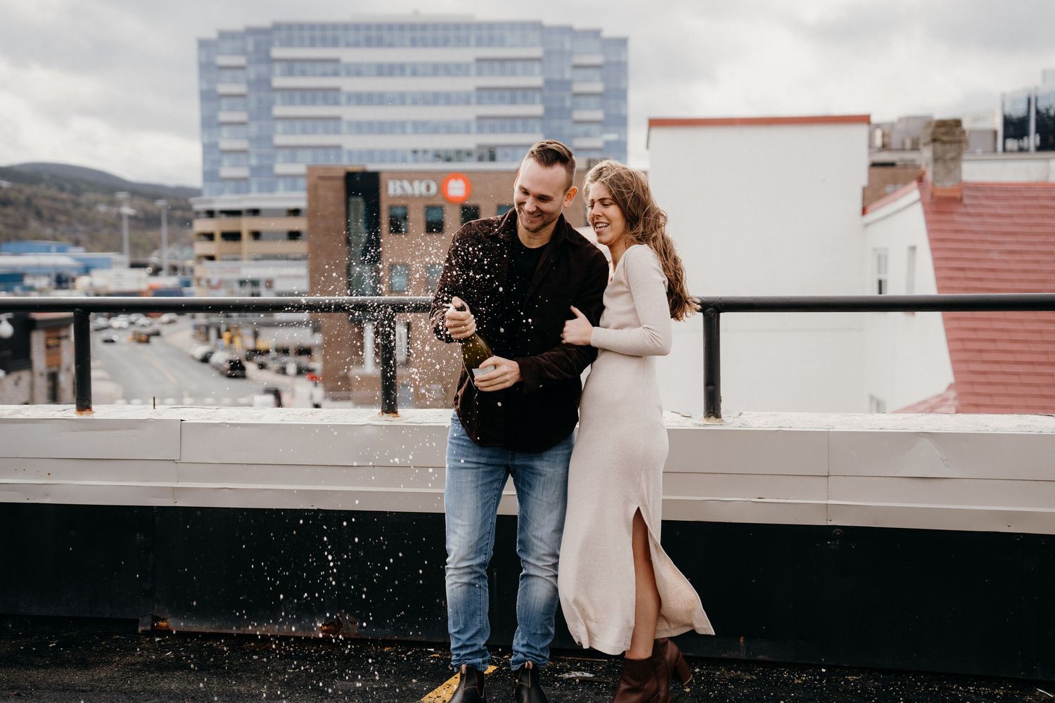A couple shares a romantic moment on an urban rooftop with city buildings in the background.