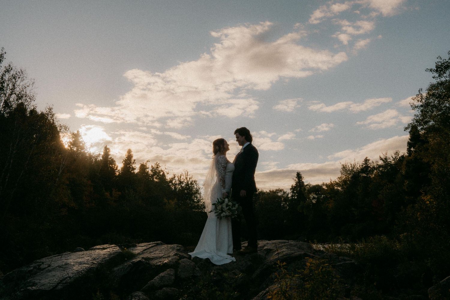 Silhouetted figures against a dramatic sunset sky with clouds and trees.
