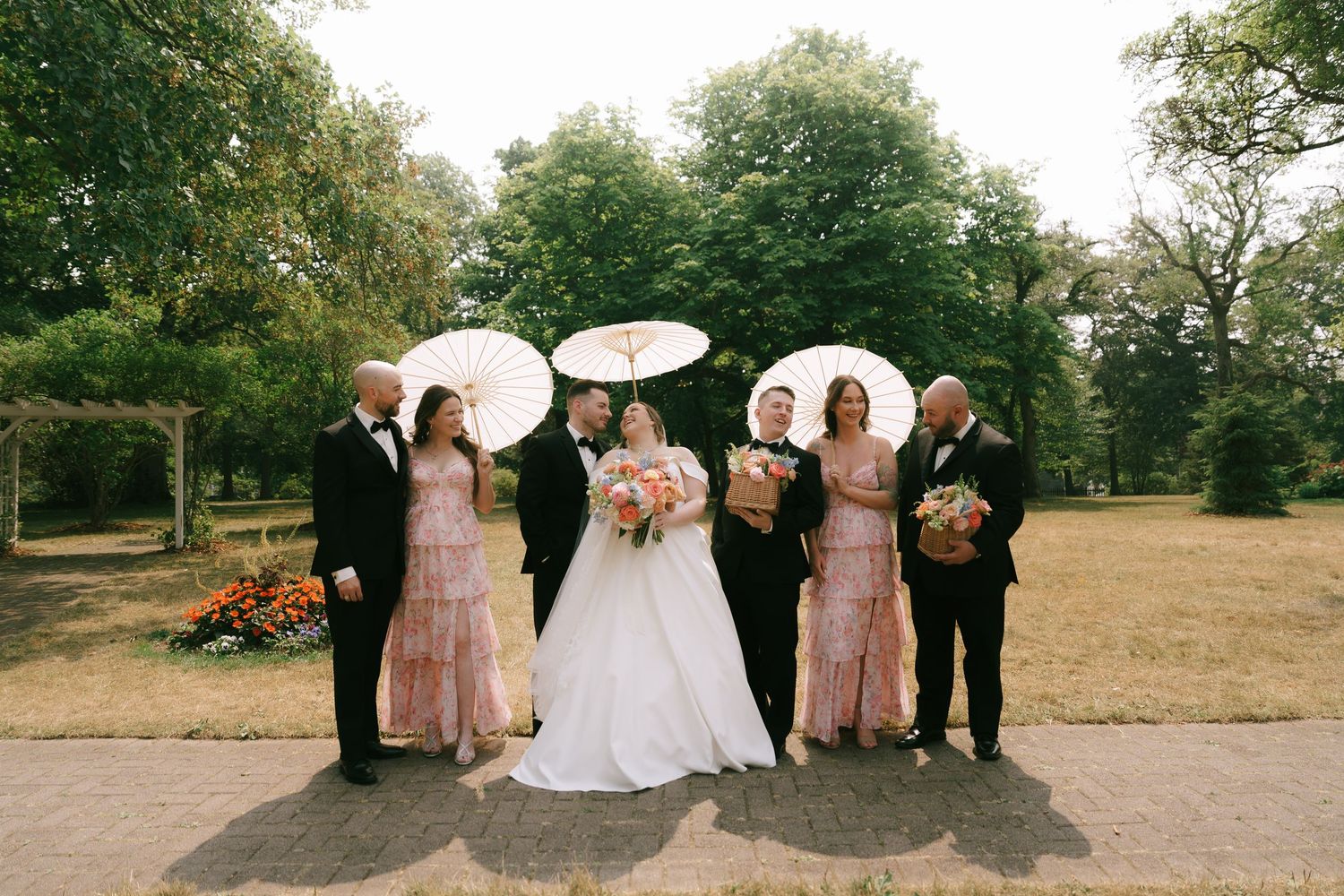 Wedding group poses together on garden path surrounded by lush greenery.