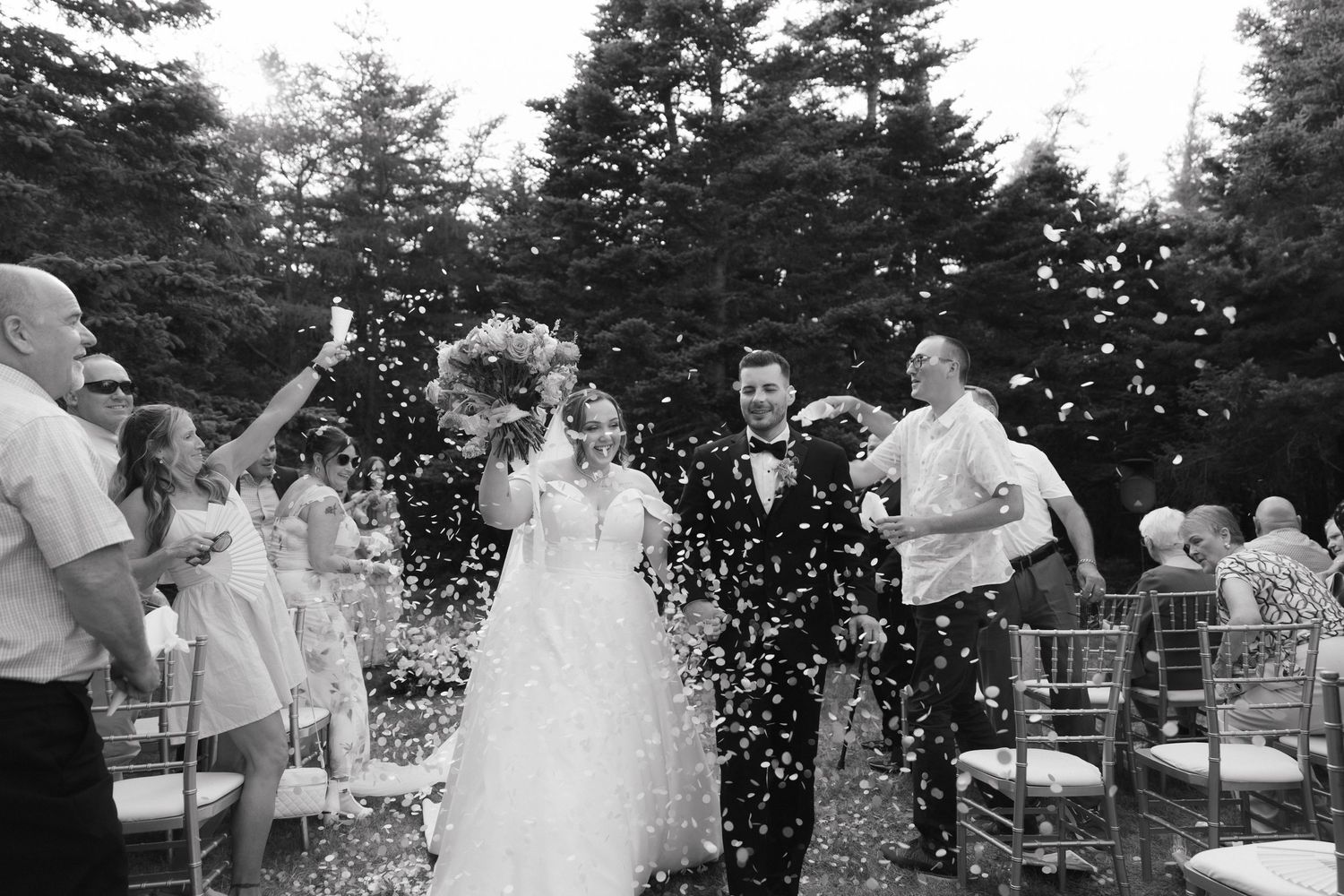 Wedding celebration with flying confetti and guests celebrating outdoors.