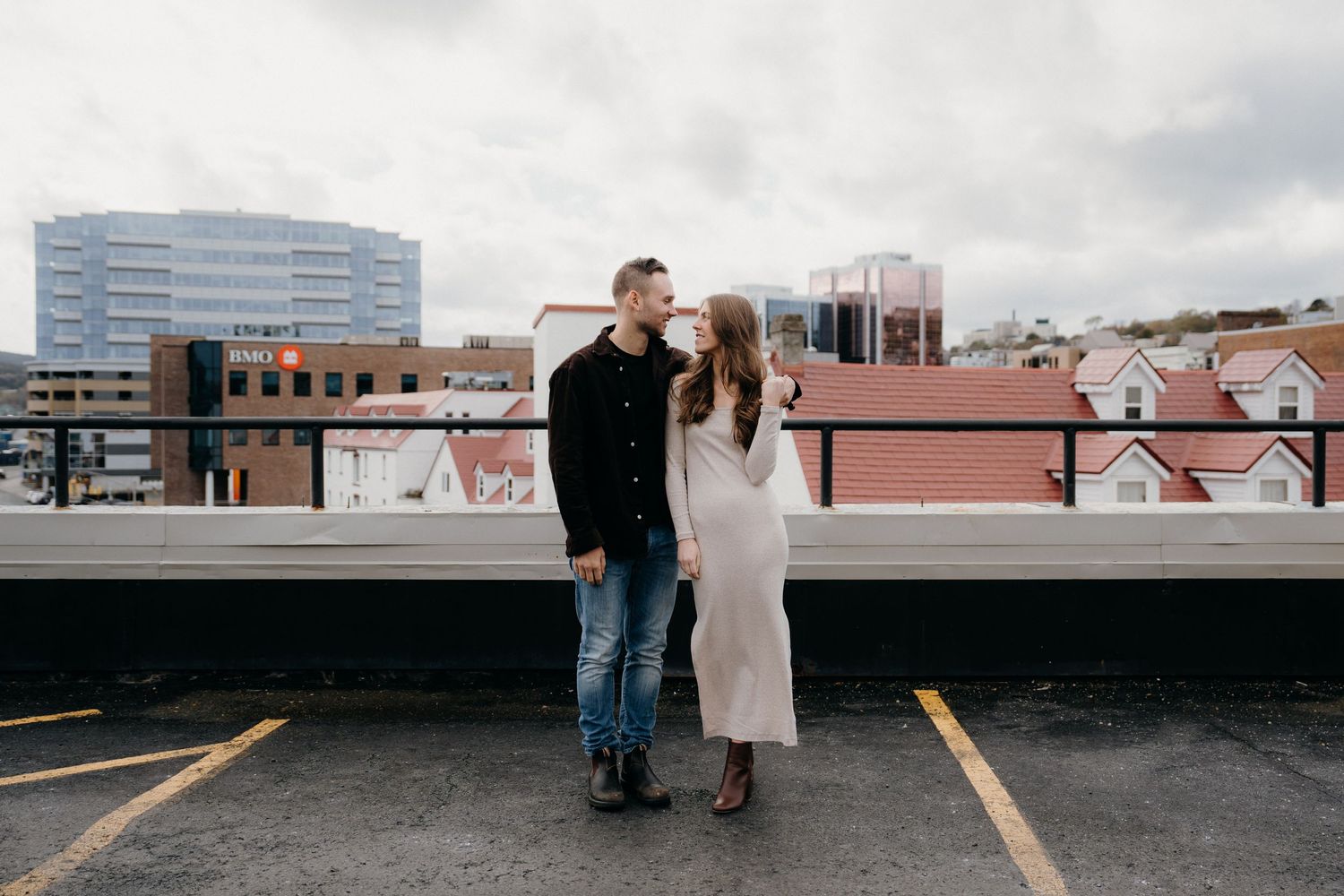 Couple sharing intimate moment on rooftop parking area with urban landscape behind them.