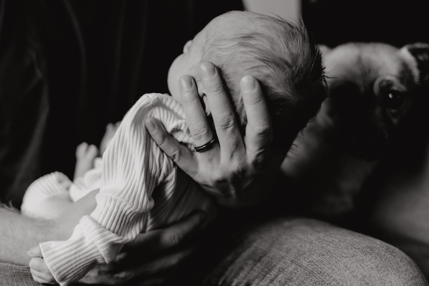 Black and white close-up of gentle hands cradling a sleeping newborn.