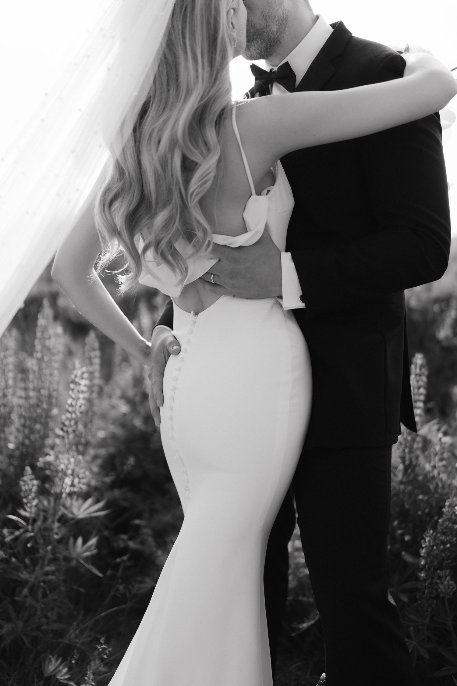 Elegant couple embraces outdoors in black and white photography.