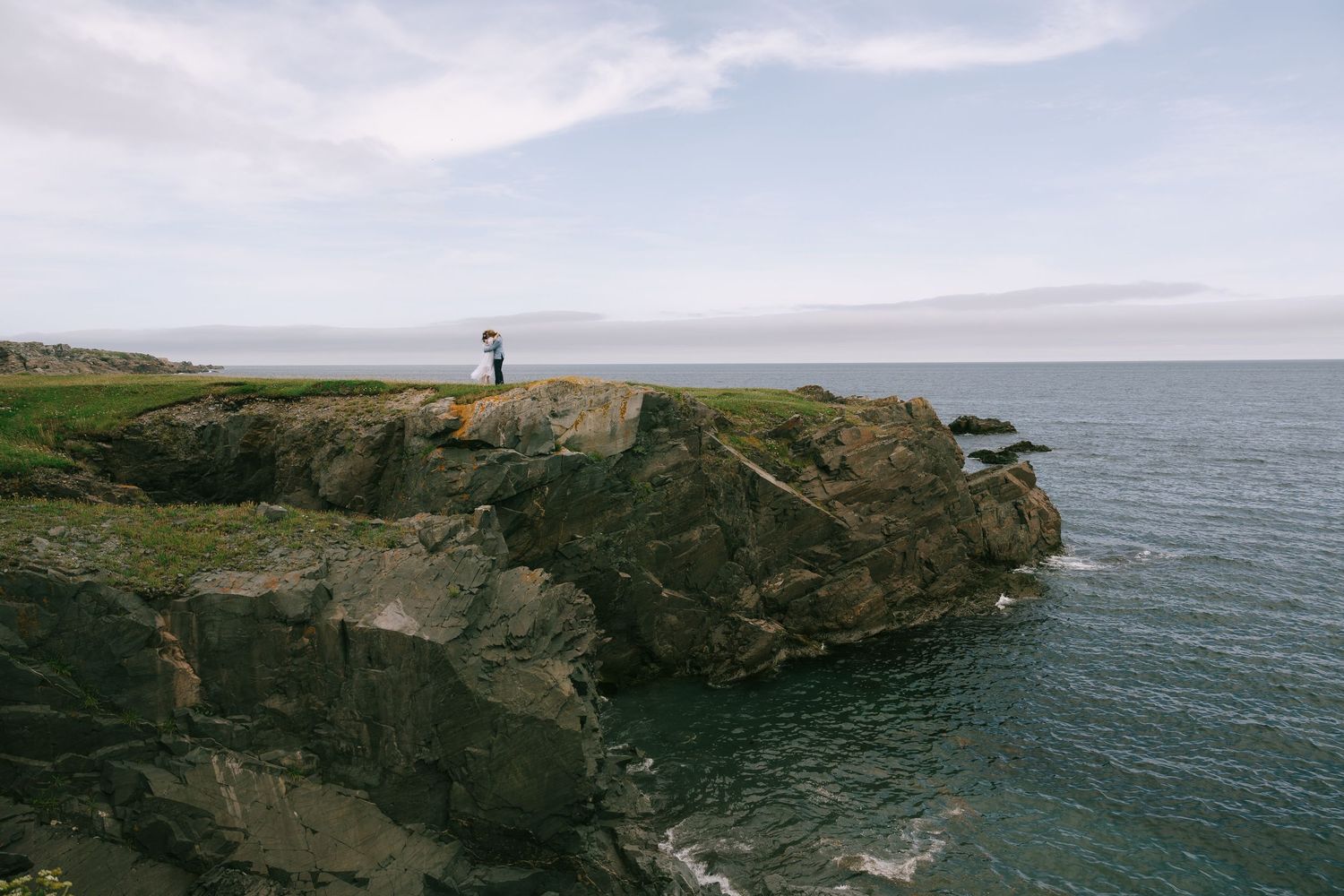Panoramic view of rugged coastal cliffs meeting the ocean under cloudy skies.