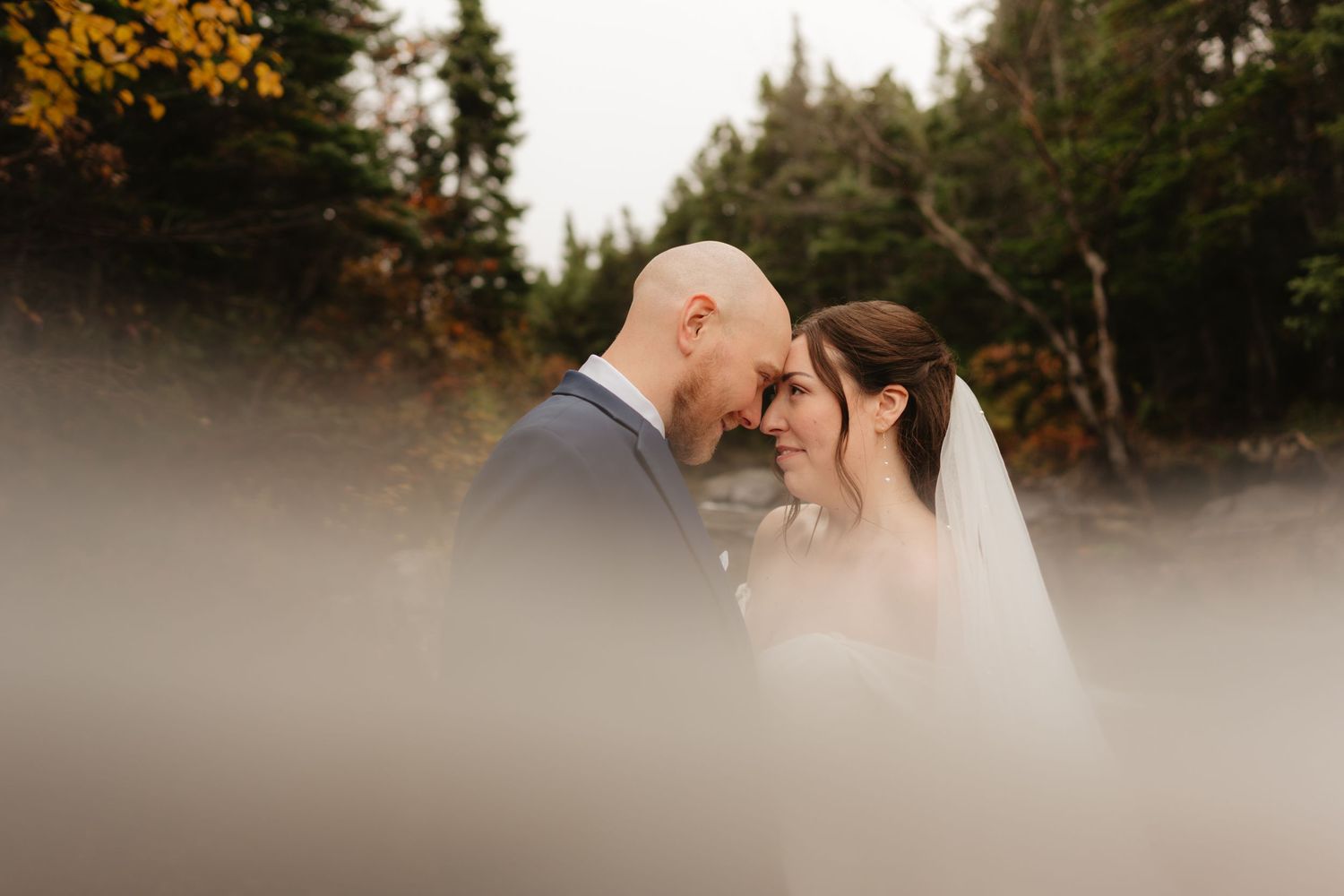 A couple shares an intimate moment during their wedding photoshoot in a misty forest setting at sunset.