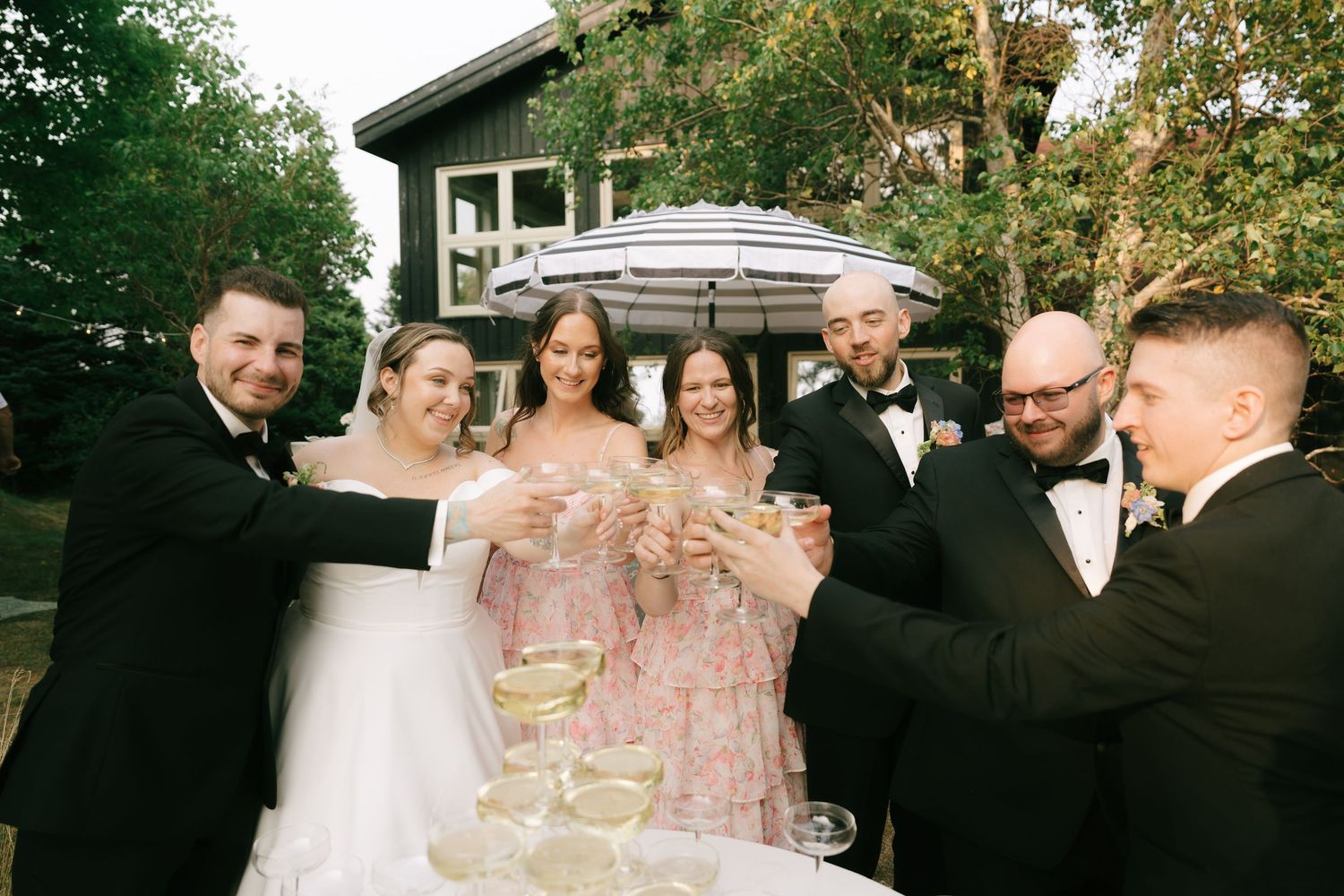 Wedding party raises champagne glasses for a group toast outdoors.