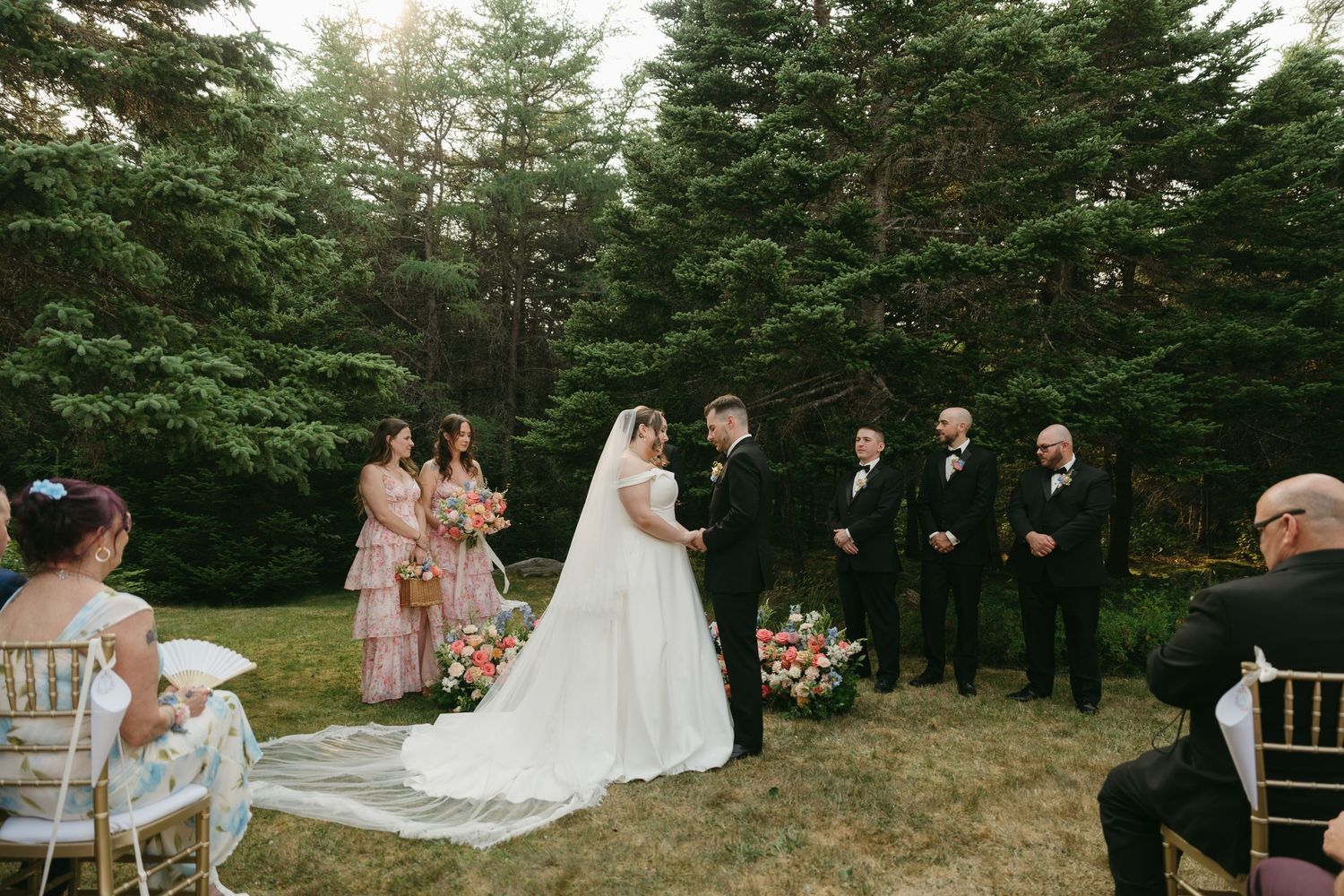 Wedding ceremony in progress with bridal party and guests gathered in a natural forest setting.