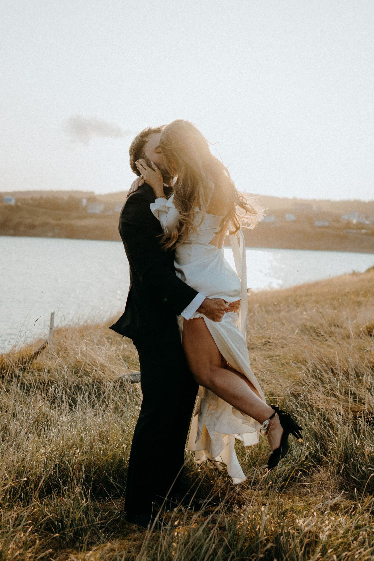 A couple embraces in a sun-drenched field during golden hour.
