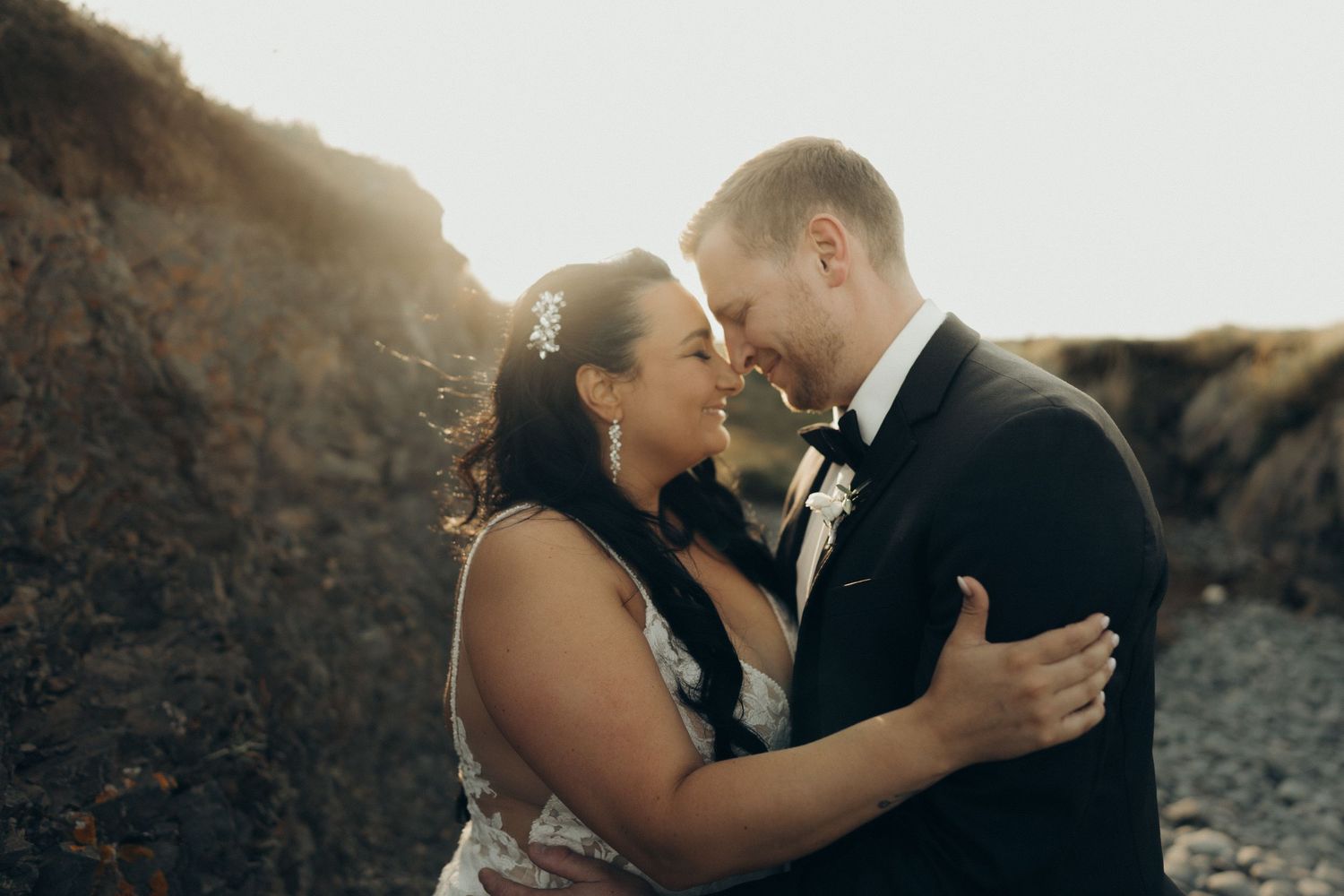 Intimate wedding moment captured in soft golden sunlight against a white background.