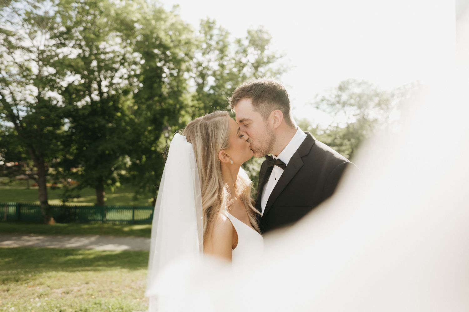 Romantic wedding couple shares tender moments in a sunlit outdoor garden setting.