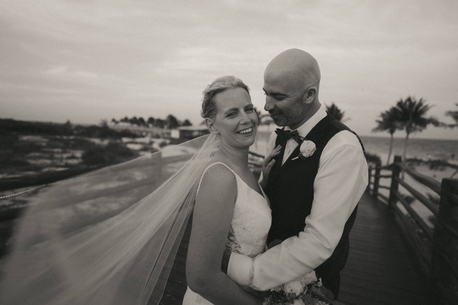 Elegant wedding portraits captured at dusk with tropical palm trees silhouetted in the background.