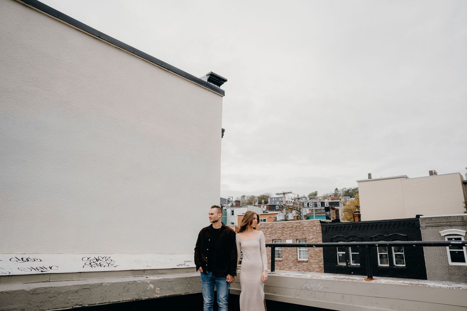 A rooftop view of an urban neighborhood with brick buildings and white walls against an overcast sky.