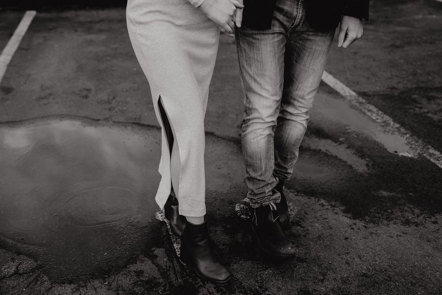 Low angle shot showing legs of couple standing close together on dark pavement.