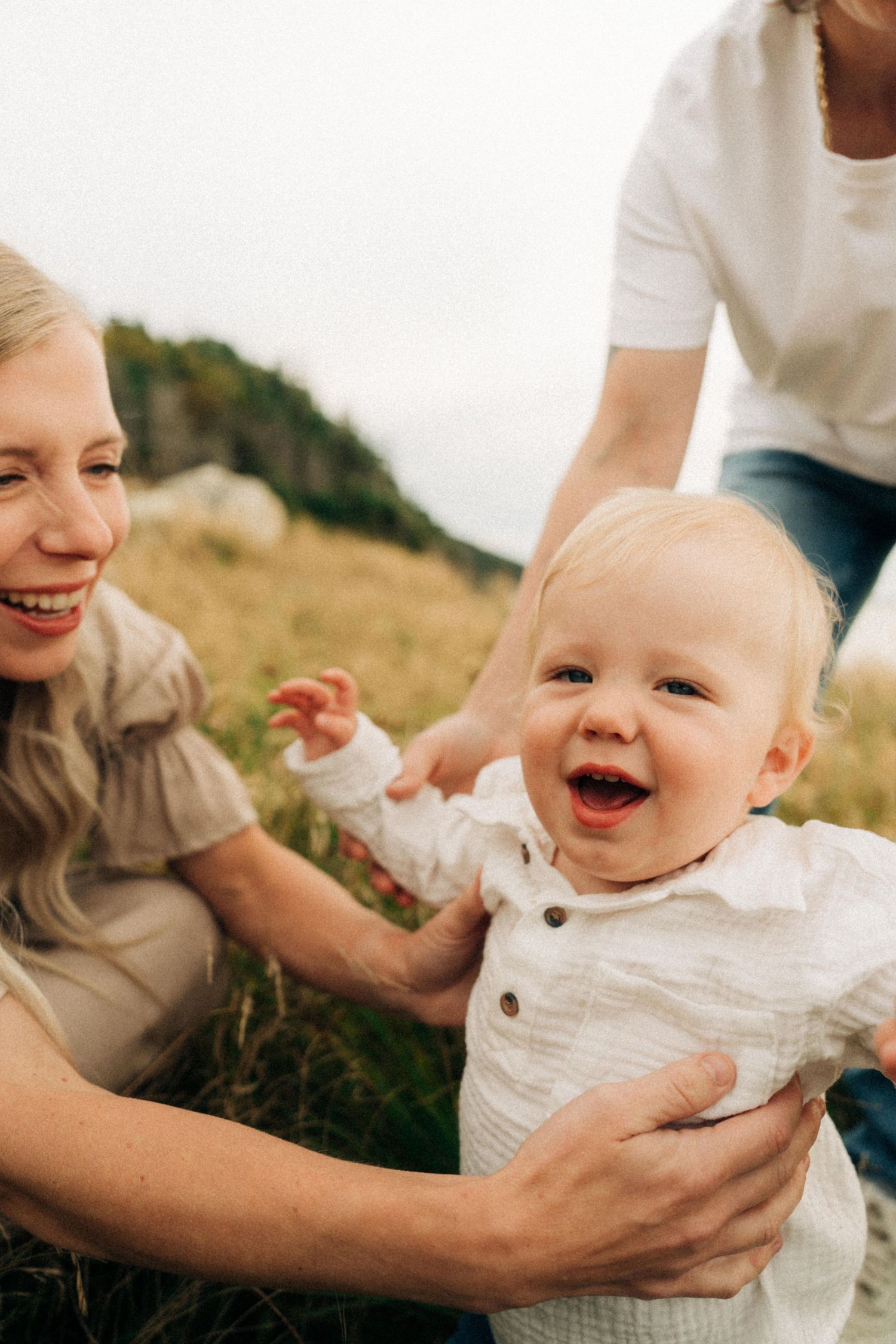 A series of candid shots showing a joyful baby in white clothing being held and playing outdoors in a grassy field.