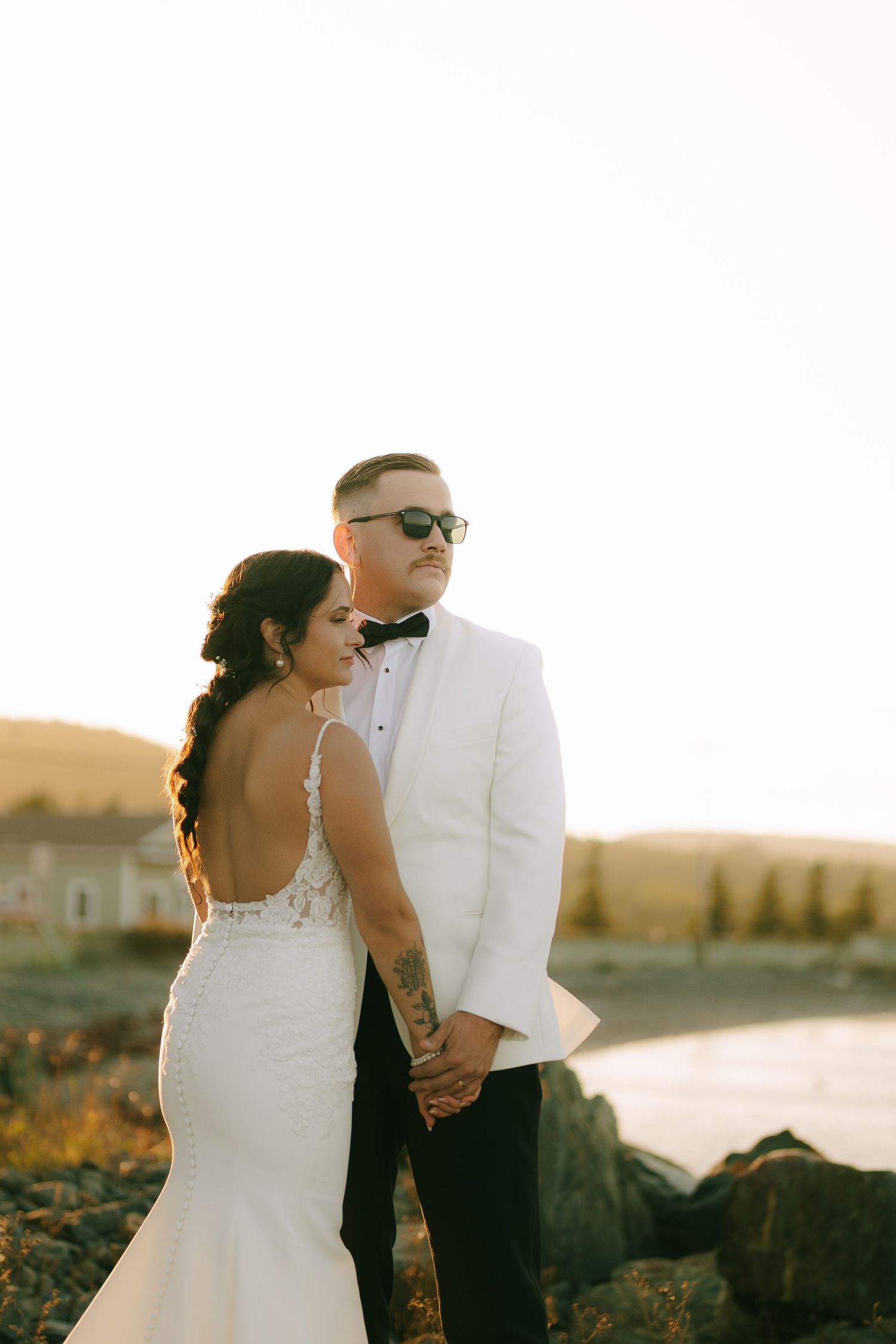 A couple in wedding attire embraces on a rocky beach at sunset in a romantic series of photos.