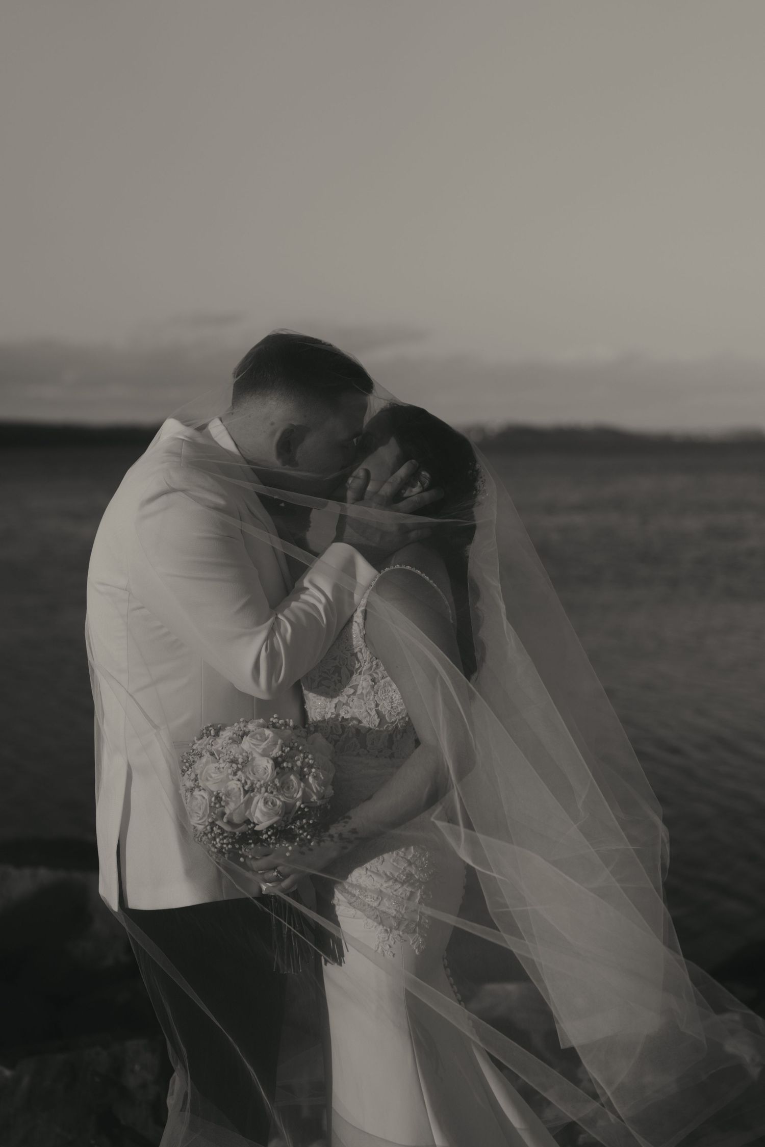 A romantic black and white wedding photo series showing a couple embracing on a scenic hilltop at sunset.