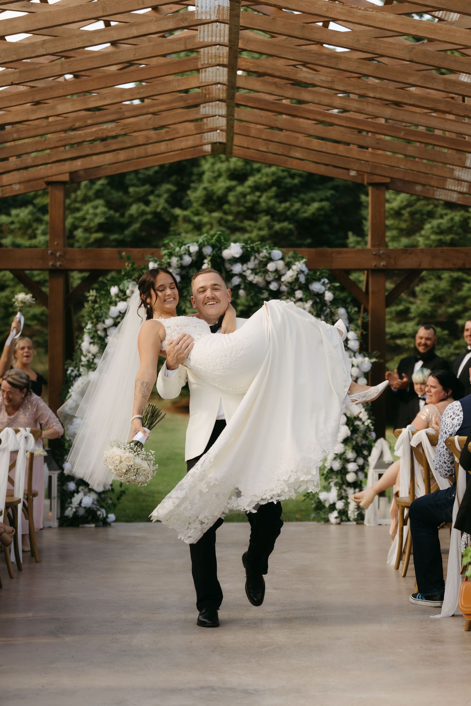 A joyous wedding celebration under a wooden pergola decorated with white floral arches as couple makes grand exit.