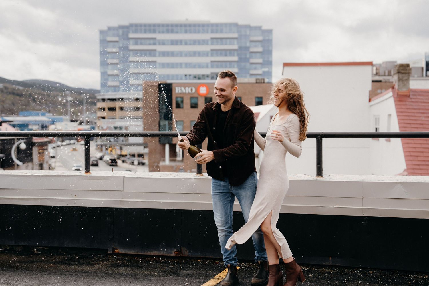 A couple shares a romantic moment on an urban rooftop with city buildings in the background.