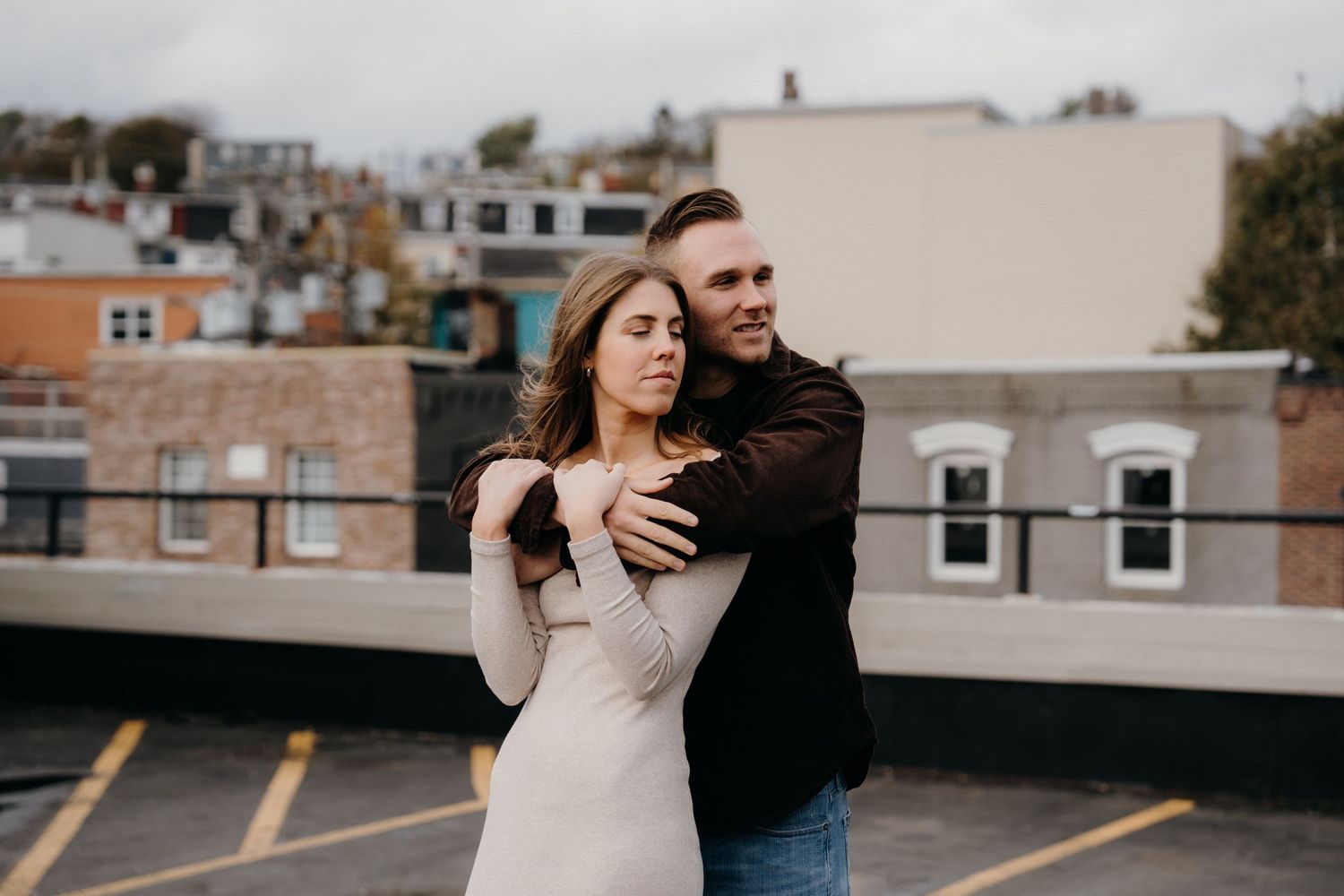 Romantic couple embraces during a casual photoshoot with city buildings in the background.