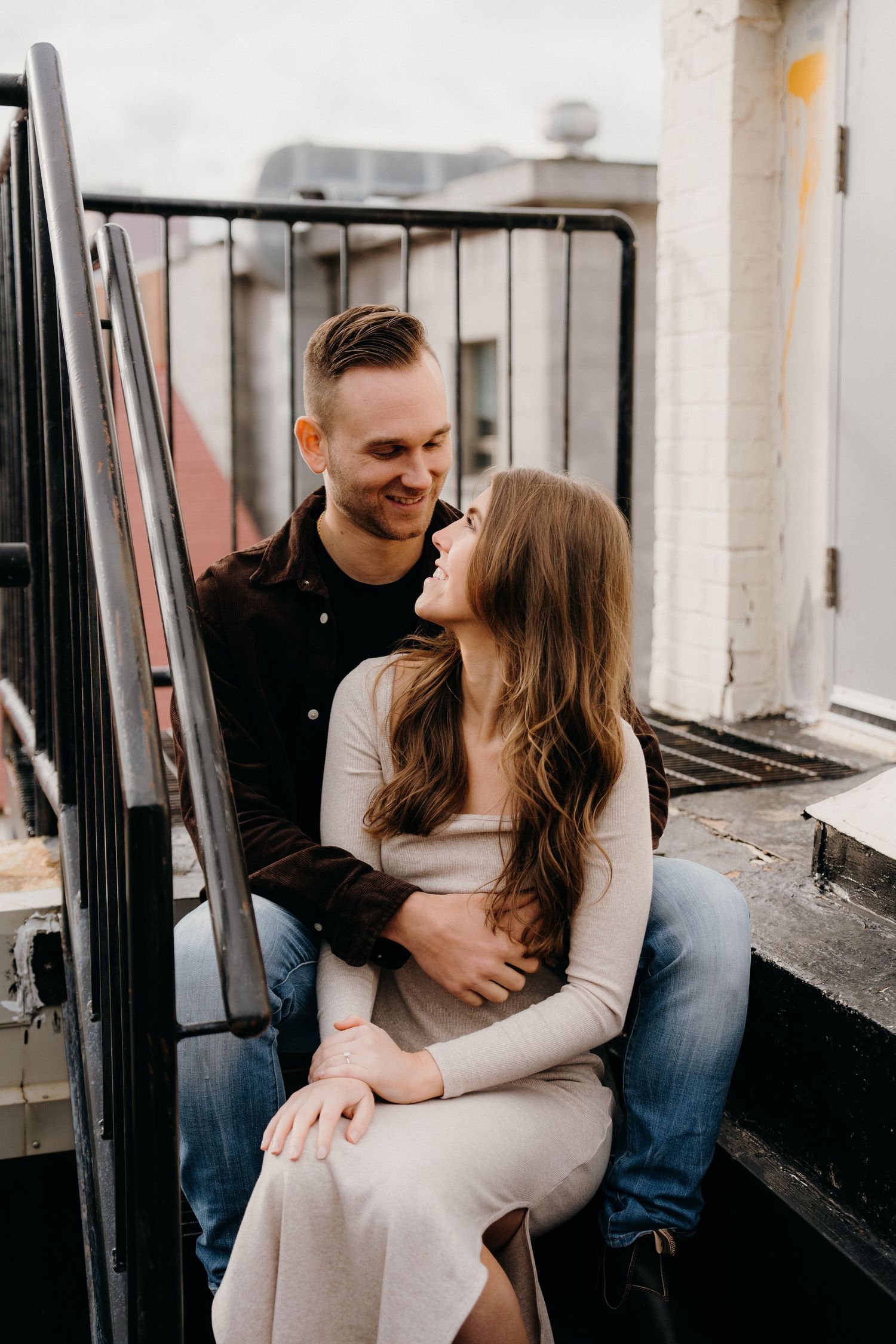 Couple sharing tender moments while sitting on industrial rooftop steps.