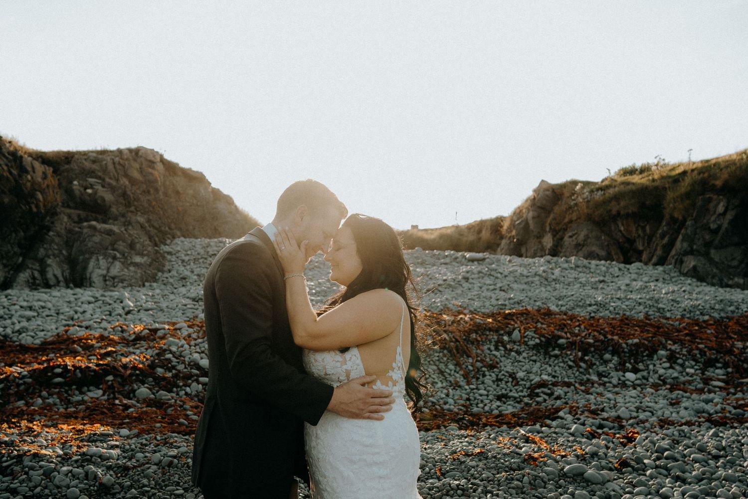 Couple sharing romantic moment on rocky beach at sunset.