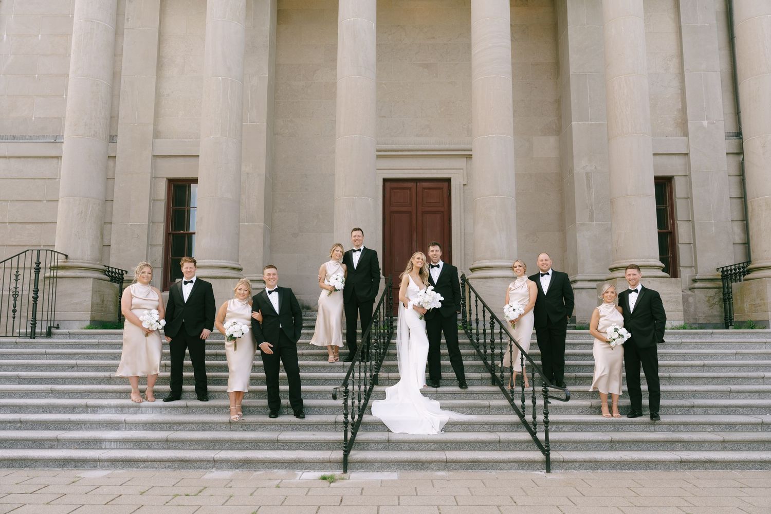 Wedding party arranged along steps of grand historic building with columns.