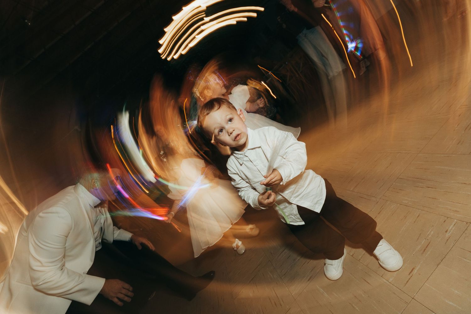 Motion blur photograph captures dancers moving on a wooden floor with dramatic light trails.