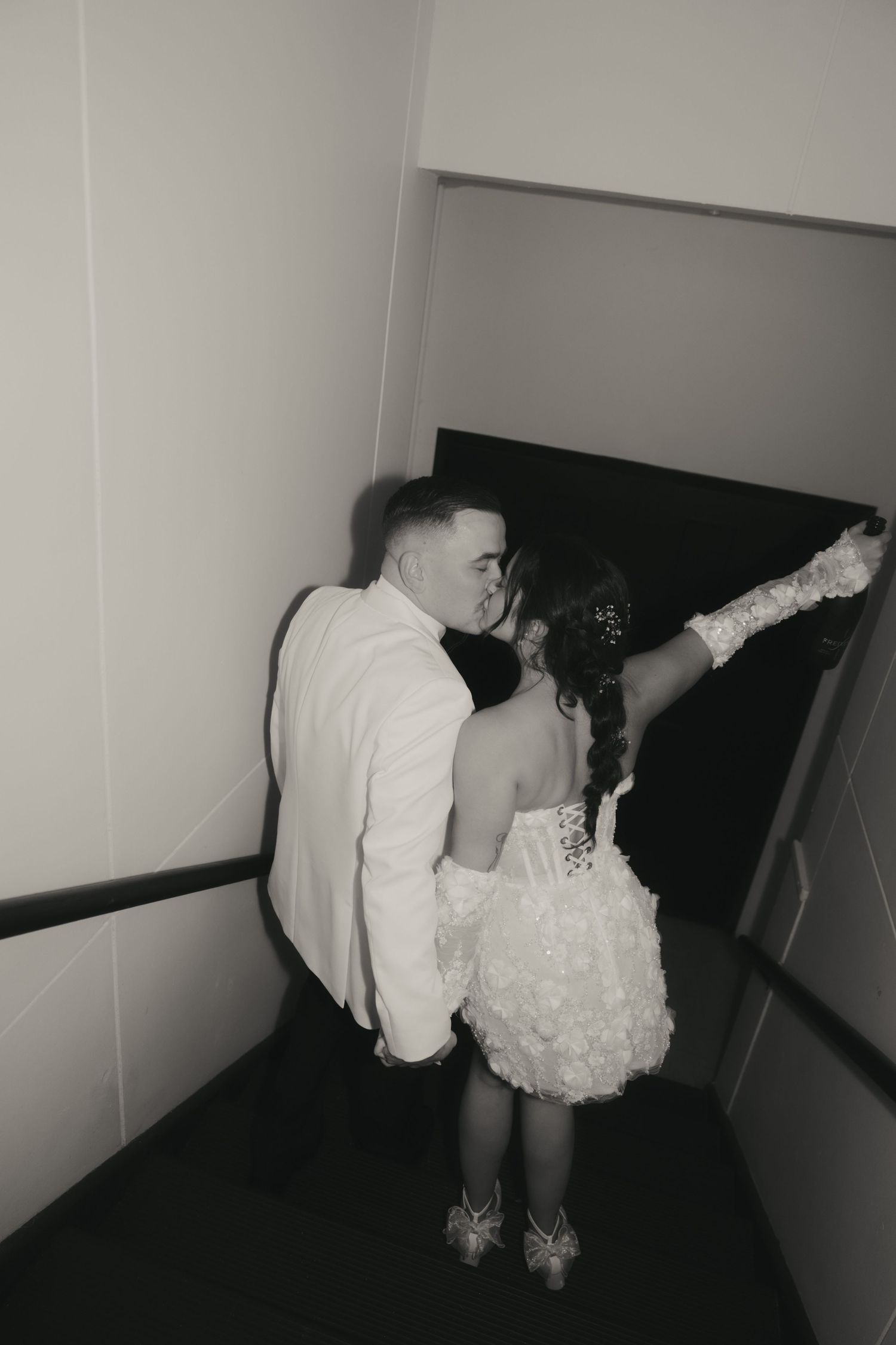 Black and white photo of a couple in formal attire dancing in a hallway, with the woman wearing a short white dress.