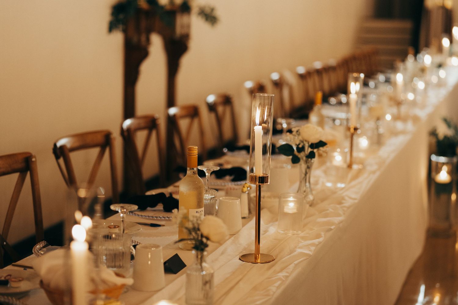 Elegant table settings with glowing candles and glassware line a long dining table at an upscale event.