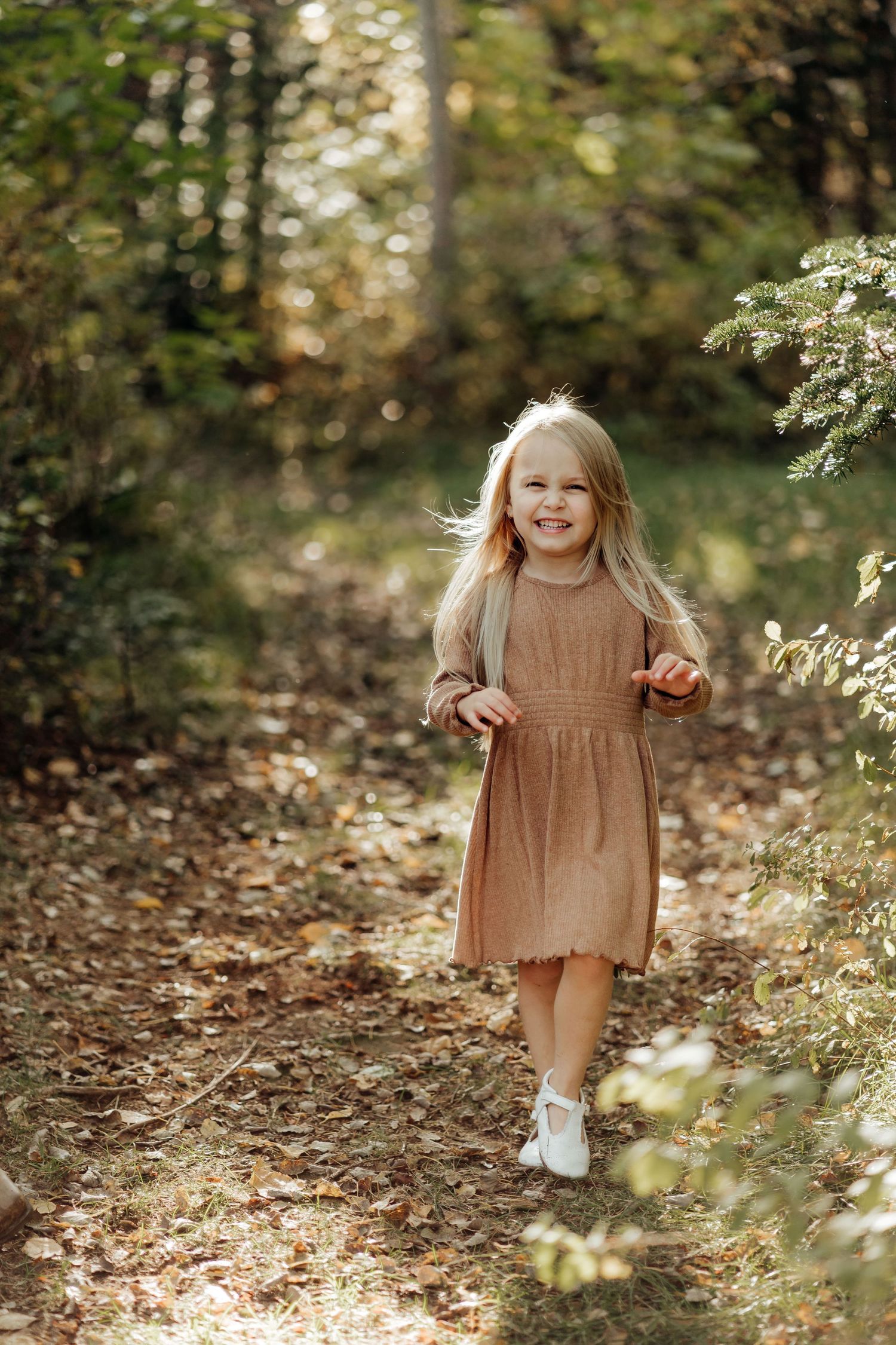 A young child in a brown dress plays joyfully among fallen autumn leaves.