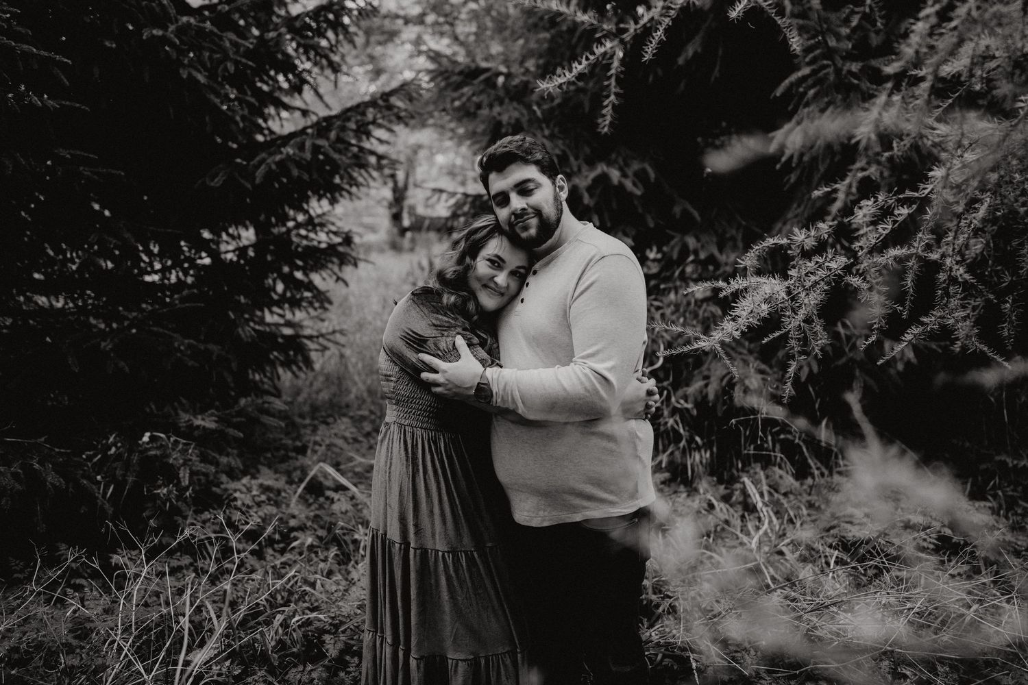 Intimate outdoor photoshoot among evergreen trees in a misty forest setting.