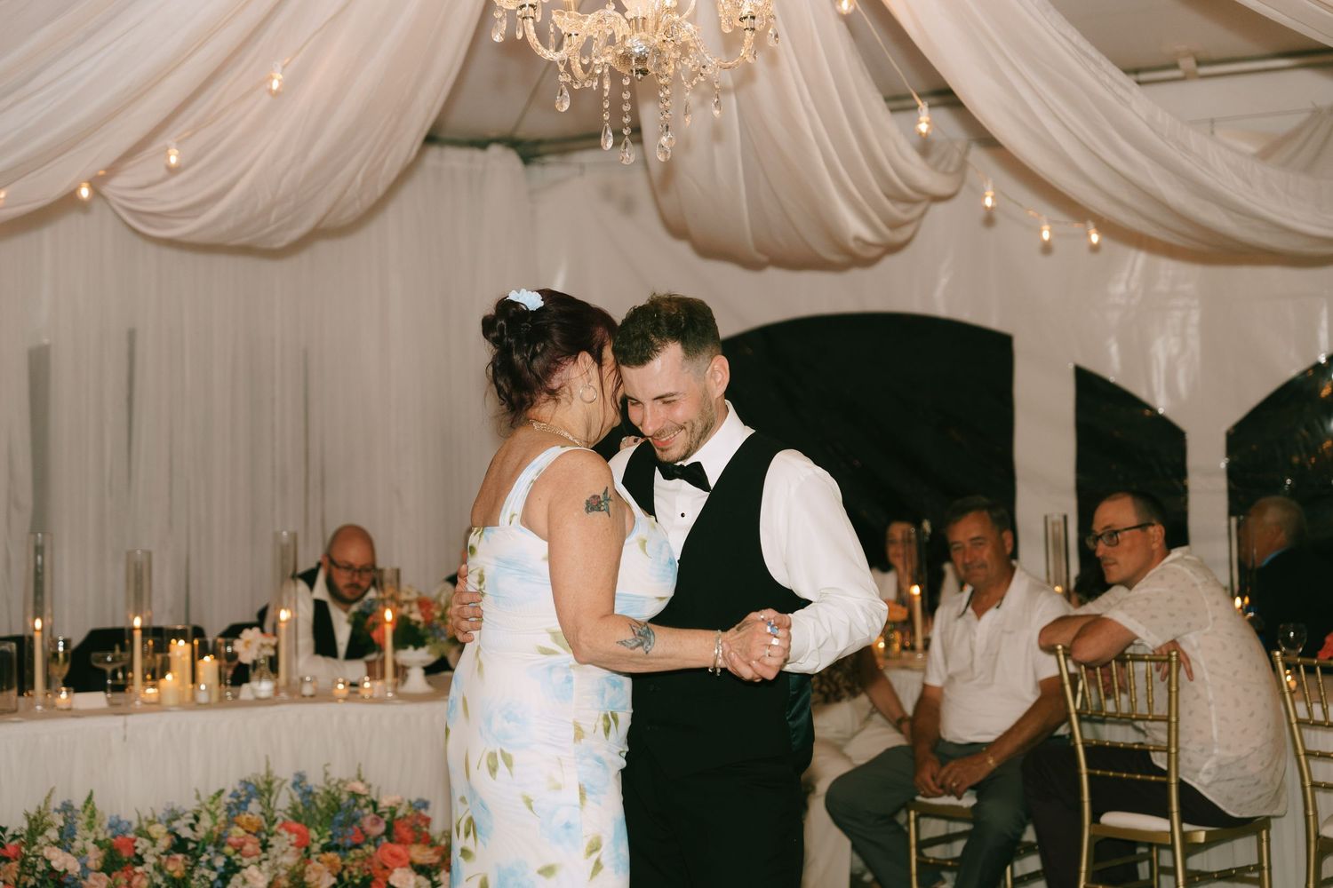Wedding guests enjoying the celebration under elegant white tent draping and chandeliers.