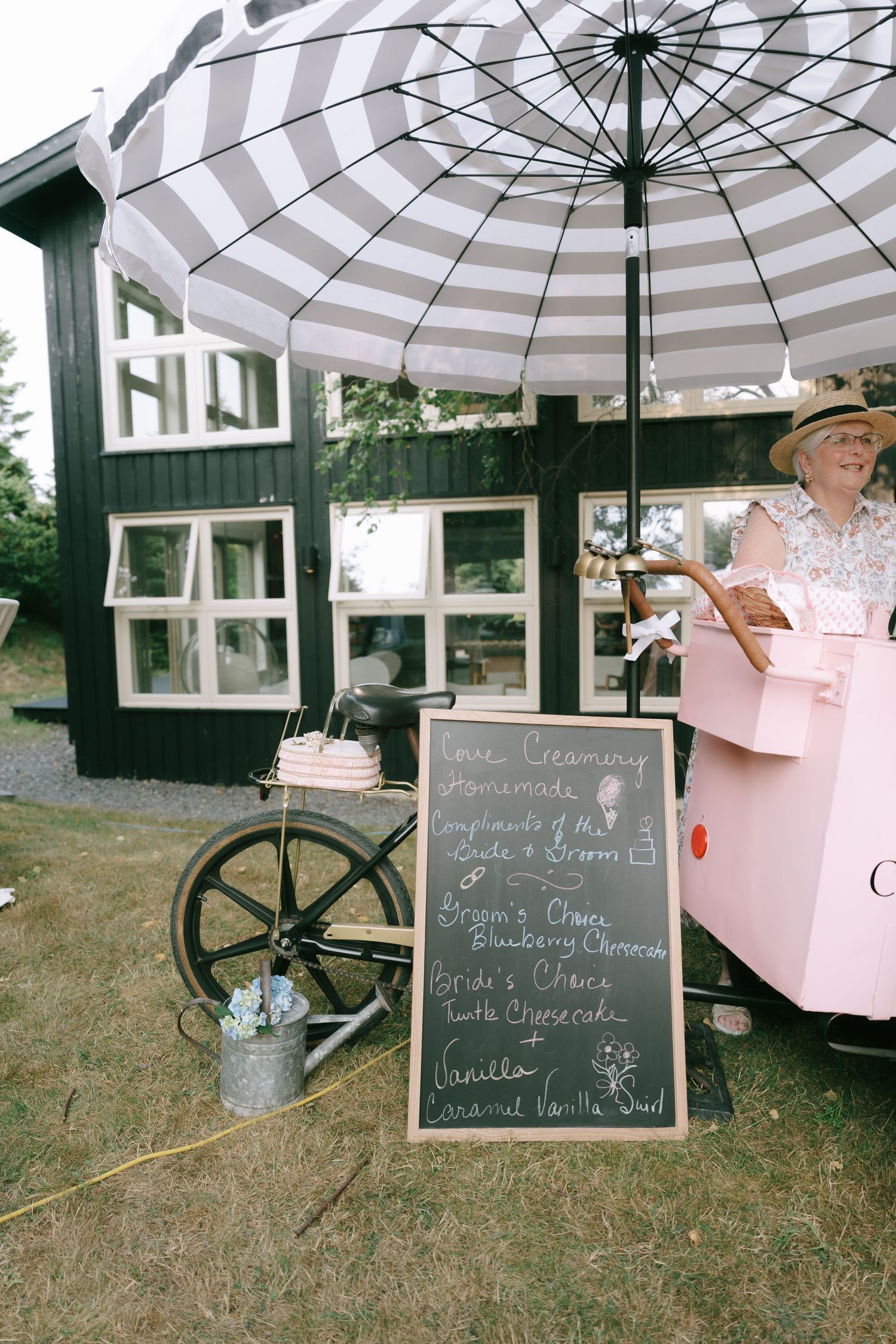 A striped umbrella shades a vintage-style drink cart with chalkboard menu signs on display.