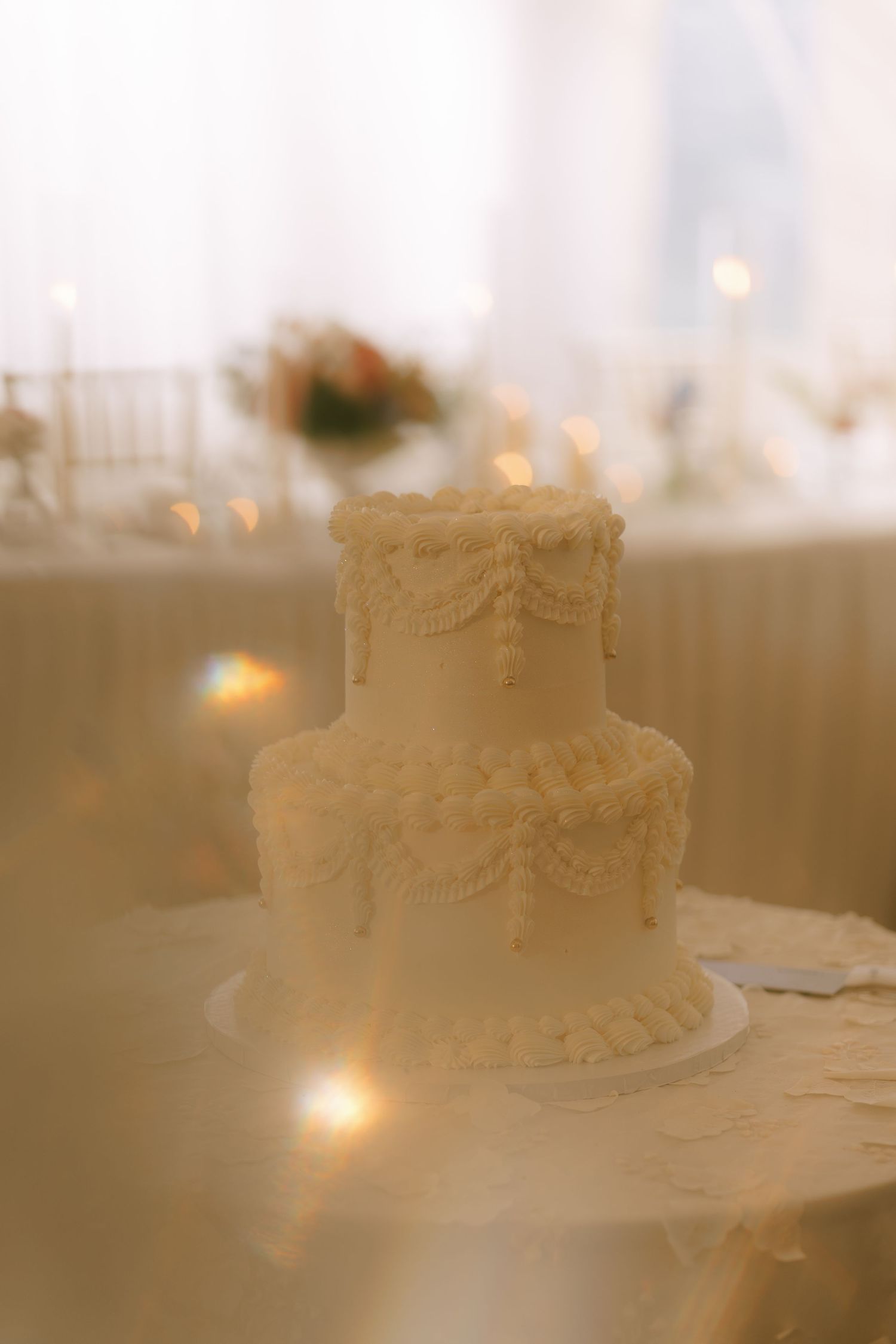 Two-tiered white wedding cake with delicate lace details captured in soft focus.